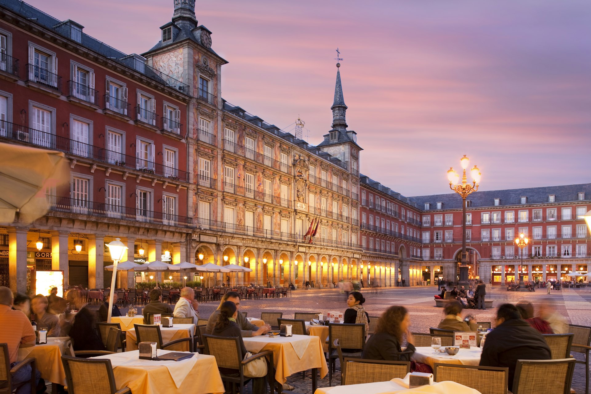 People sitting outside at tables on Madrid's Plaza Mayor at dusk