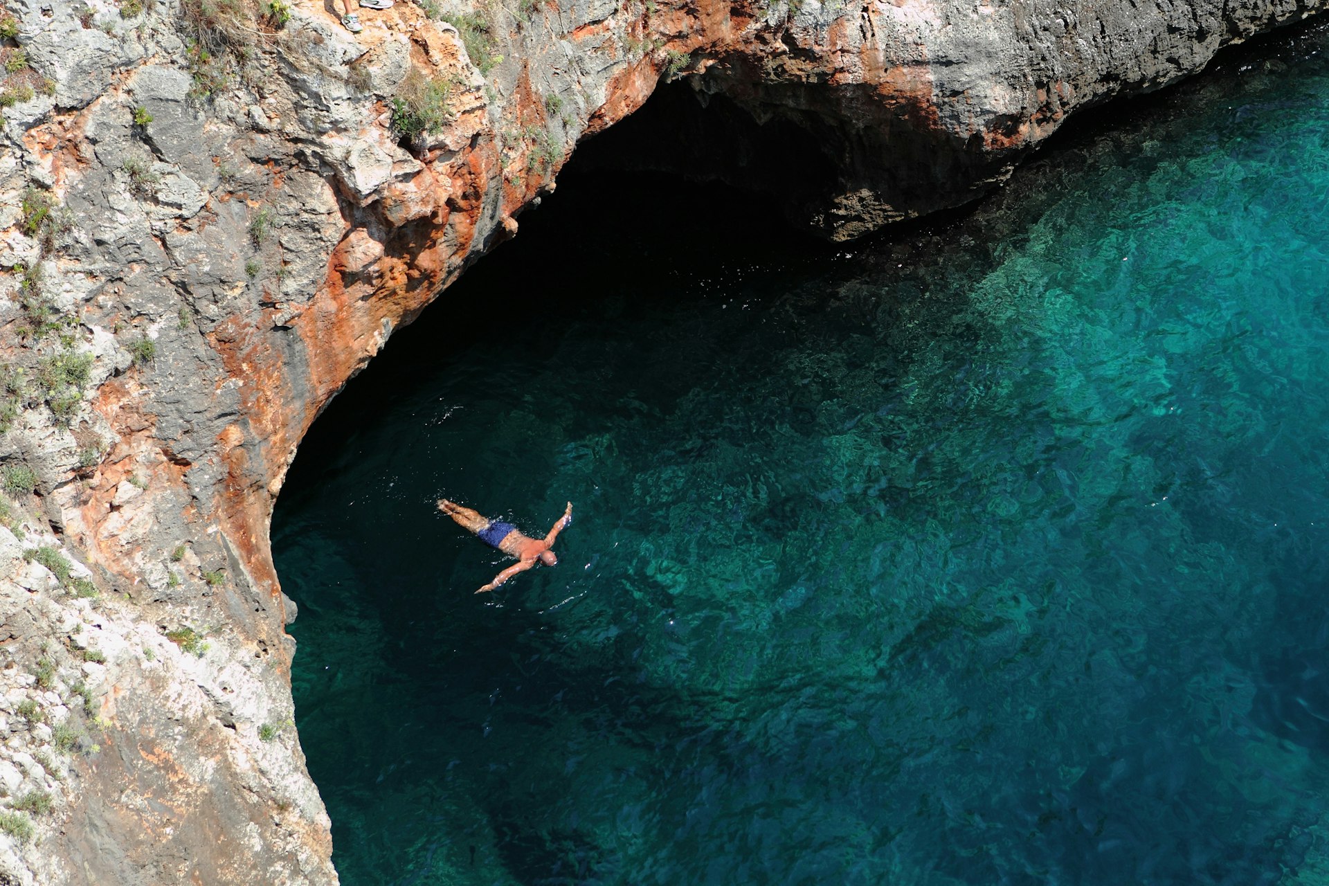 A person floats in a bay surrounded by rock