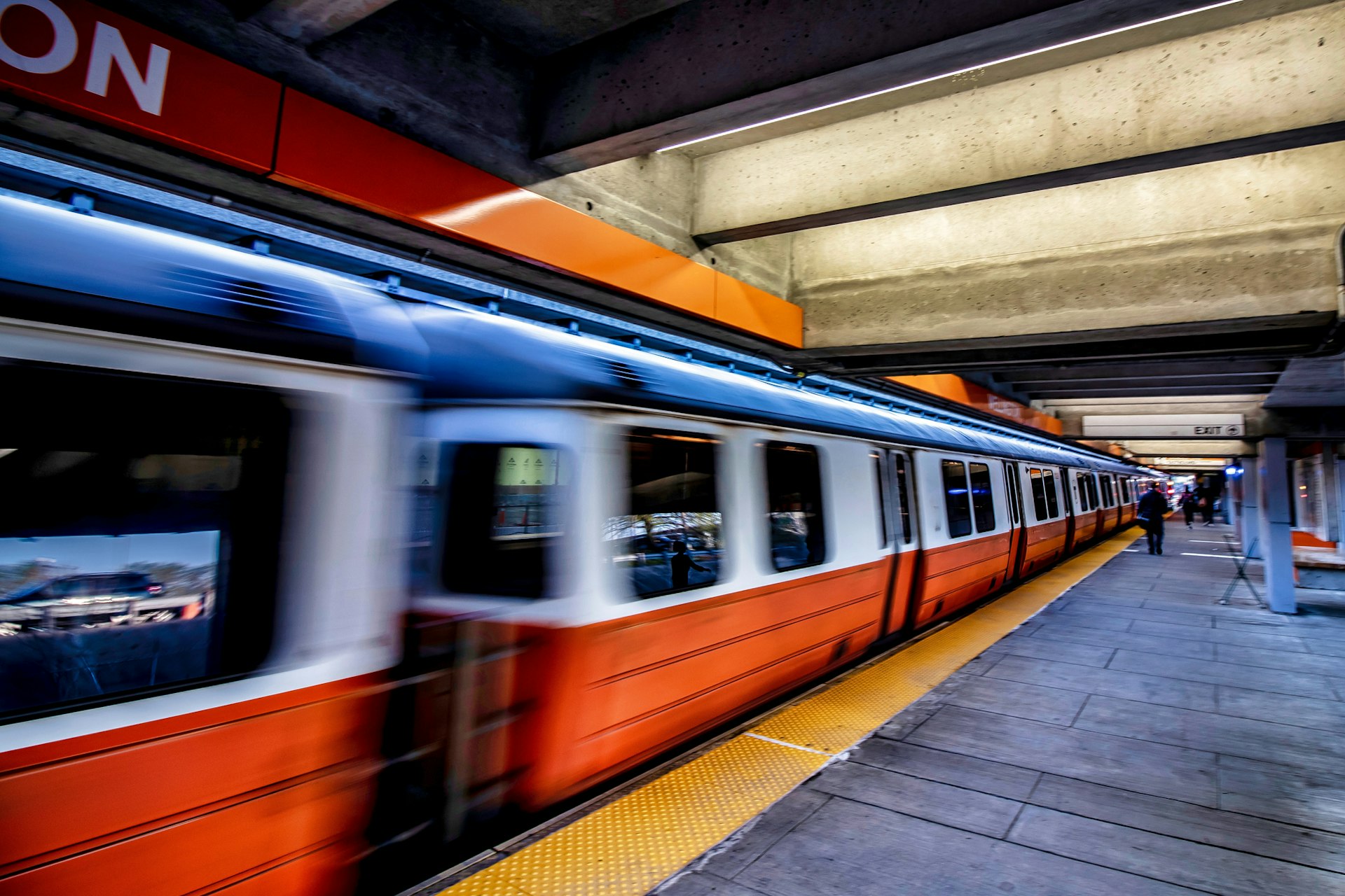 A subway train passes through a station as a person walks along the platform