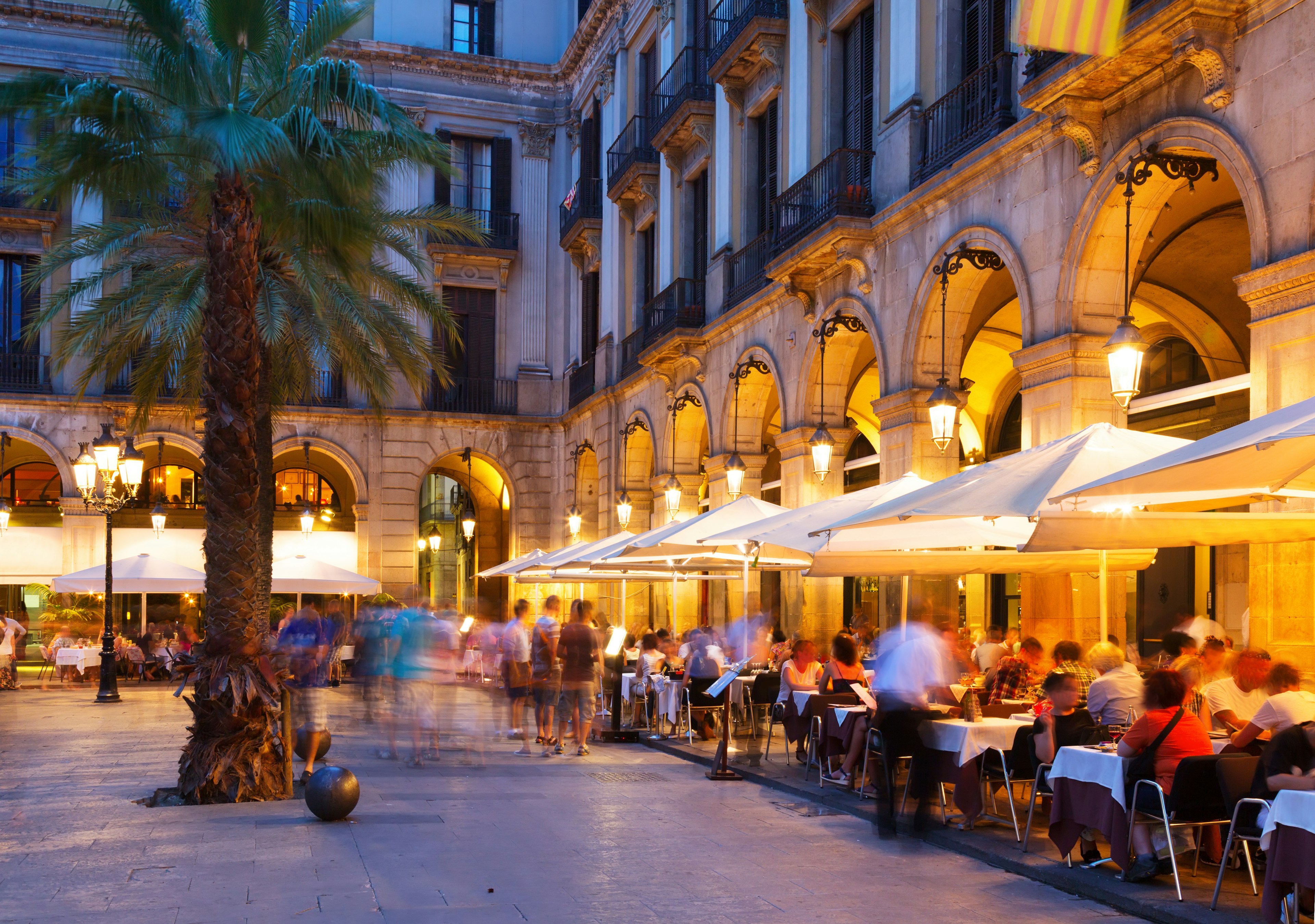 People sit at restaurant tables in a square in the evening