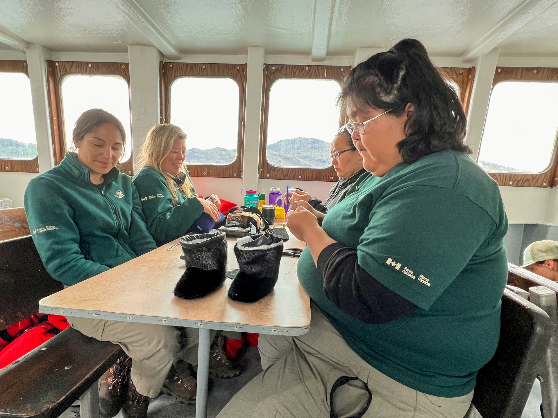 People sit around a table on a boat sewing small boots