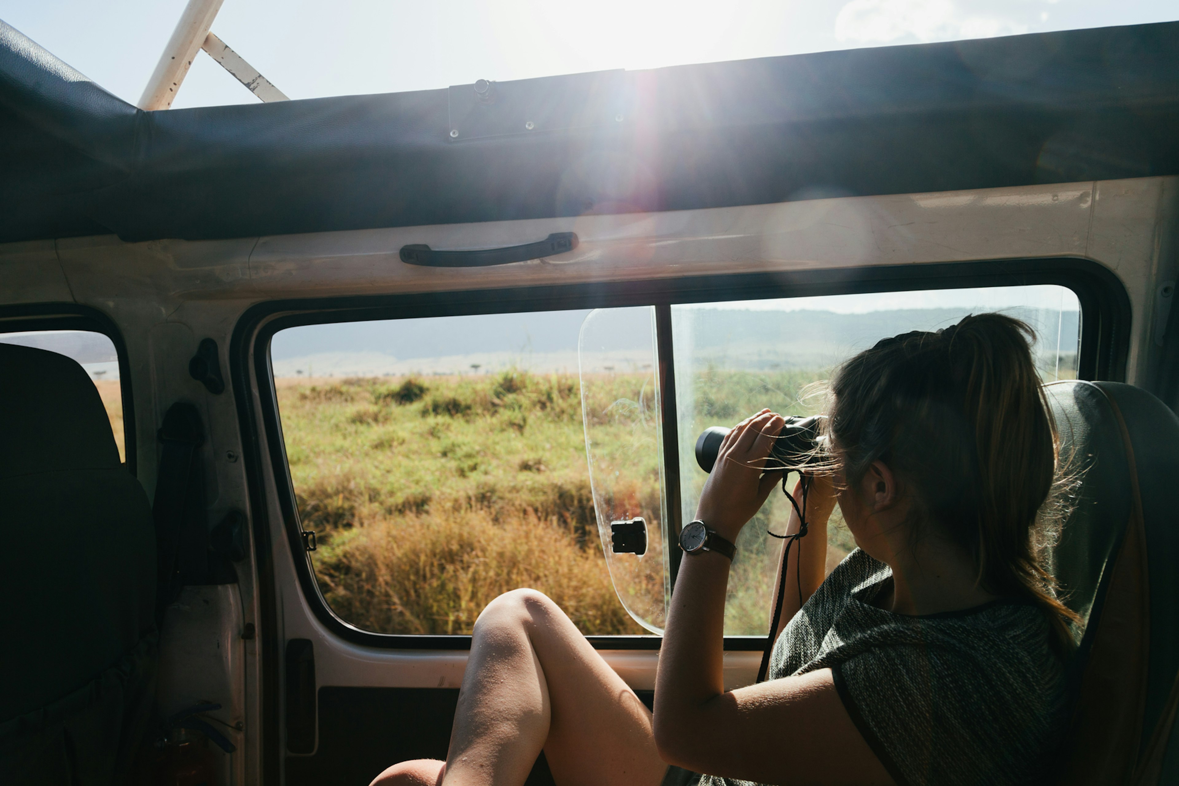 woman looking out on savannah with binoculars from truck