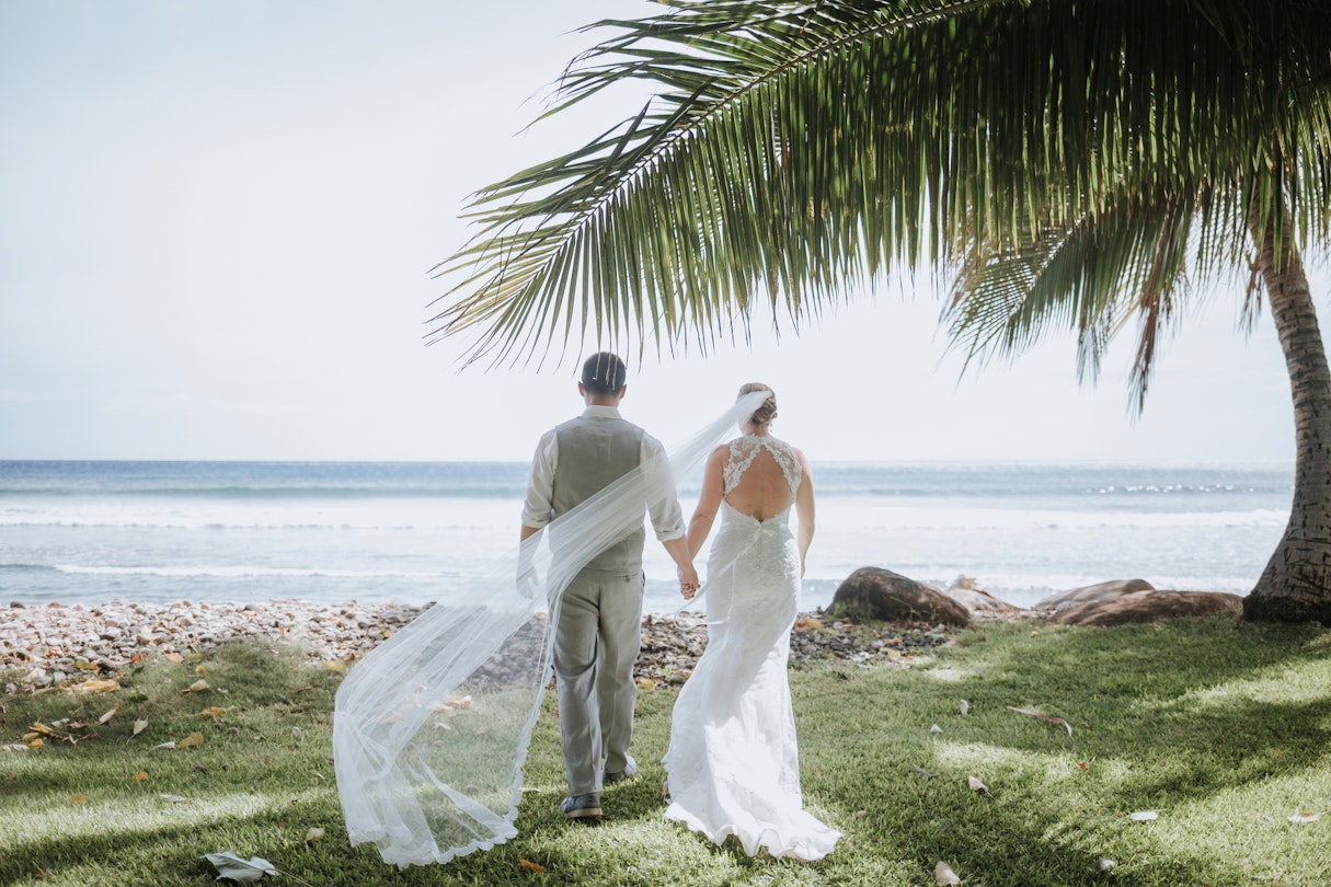 Wedding Couple Walking towards Ocean with Breeze Catching Veil
