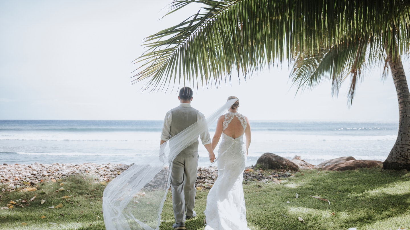 Wedding Couple Walking towards Ocean with Breeze Catching Veil