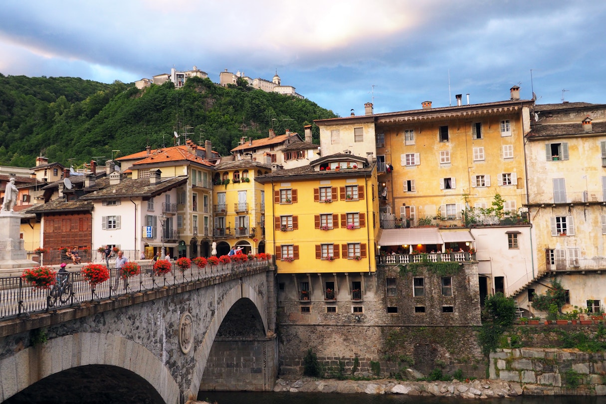 View of bridge over Mastallone river, red geraniums on railing. Ancient mountain town, in the Italian region of Piedmont, cloudy evening mood with Sacro Monte buildings on the hill behind. Important tourist resort.
1091344436