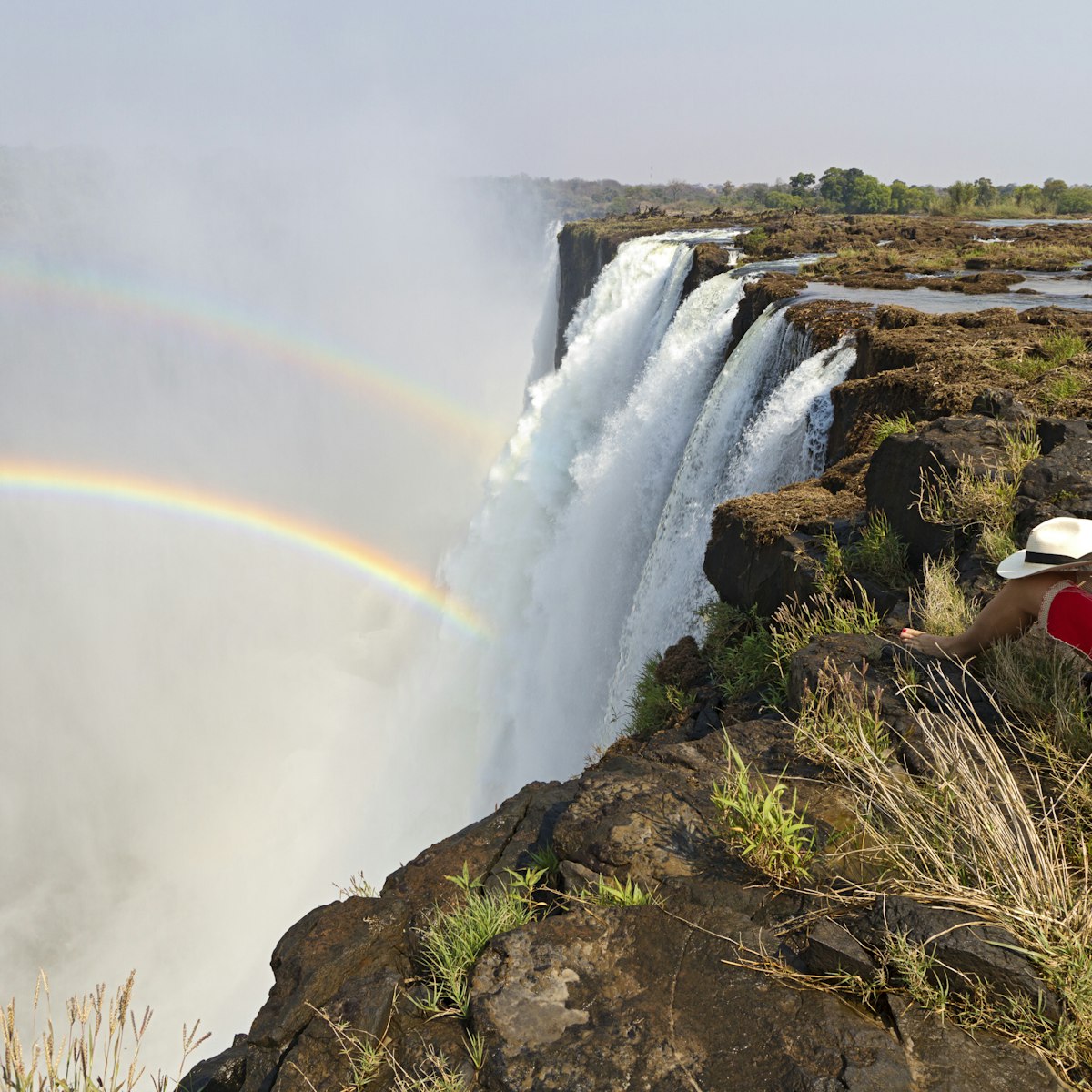 Young woman sitting at the edge of Victoria Falls, Livingstone, Zambia, Africa