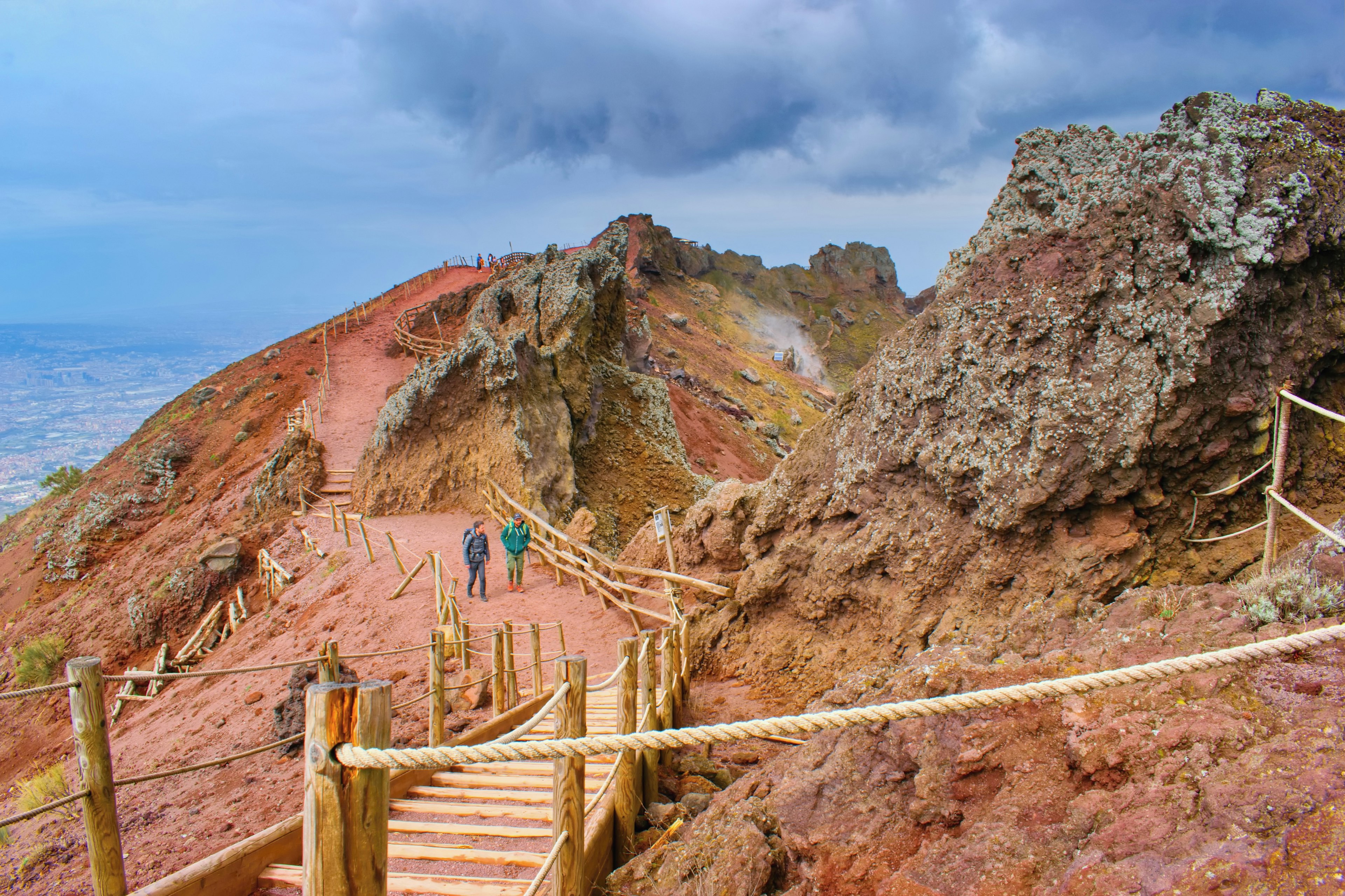 Two hikers follow a marked trail through a red rocky landscape