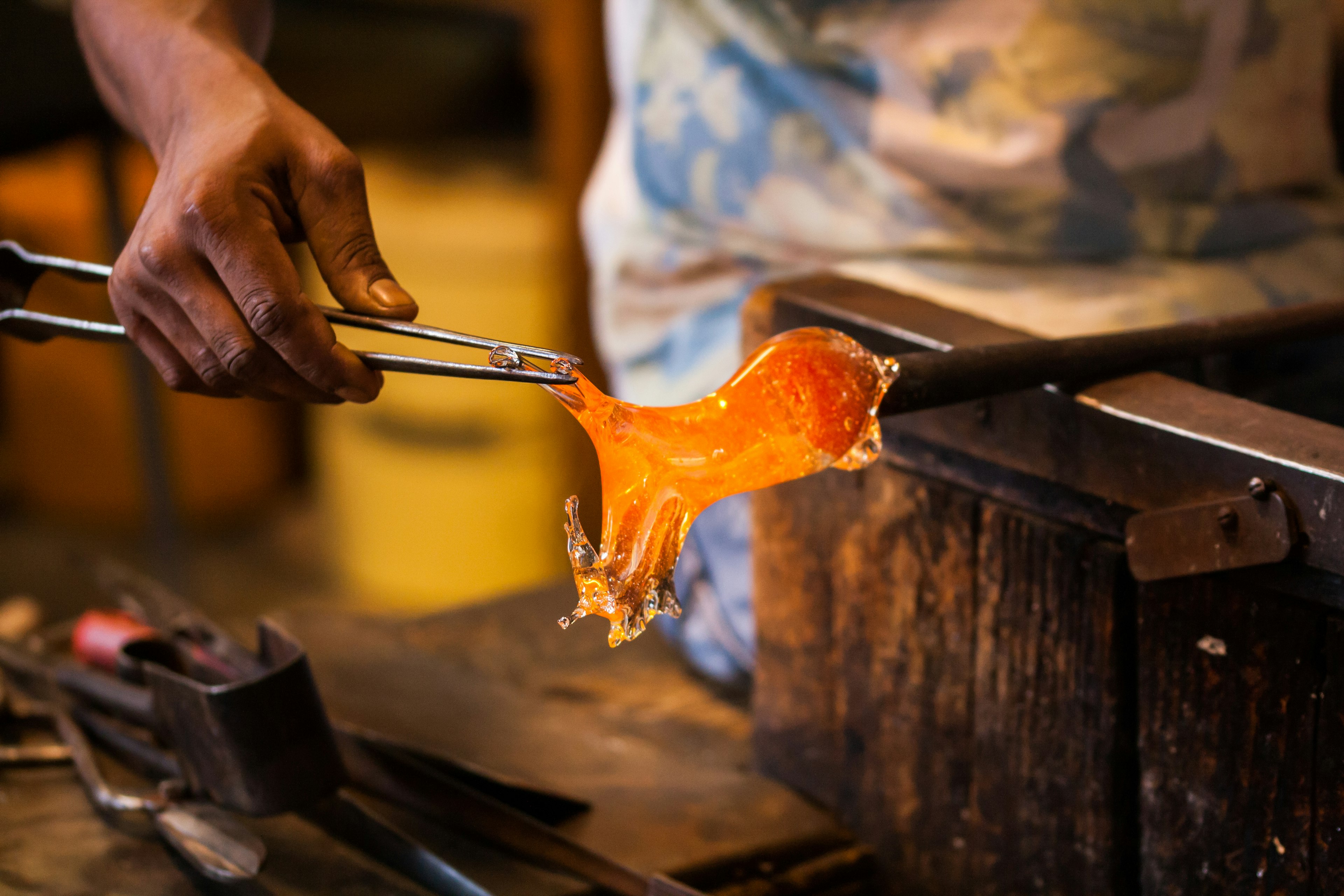 An artisan works some molten glass into shape in a glass-blowing workshop