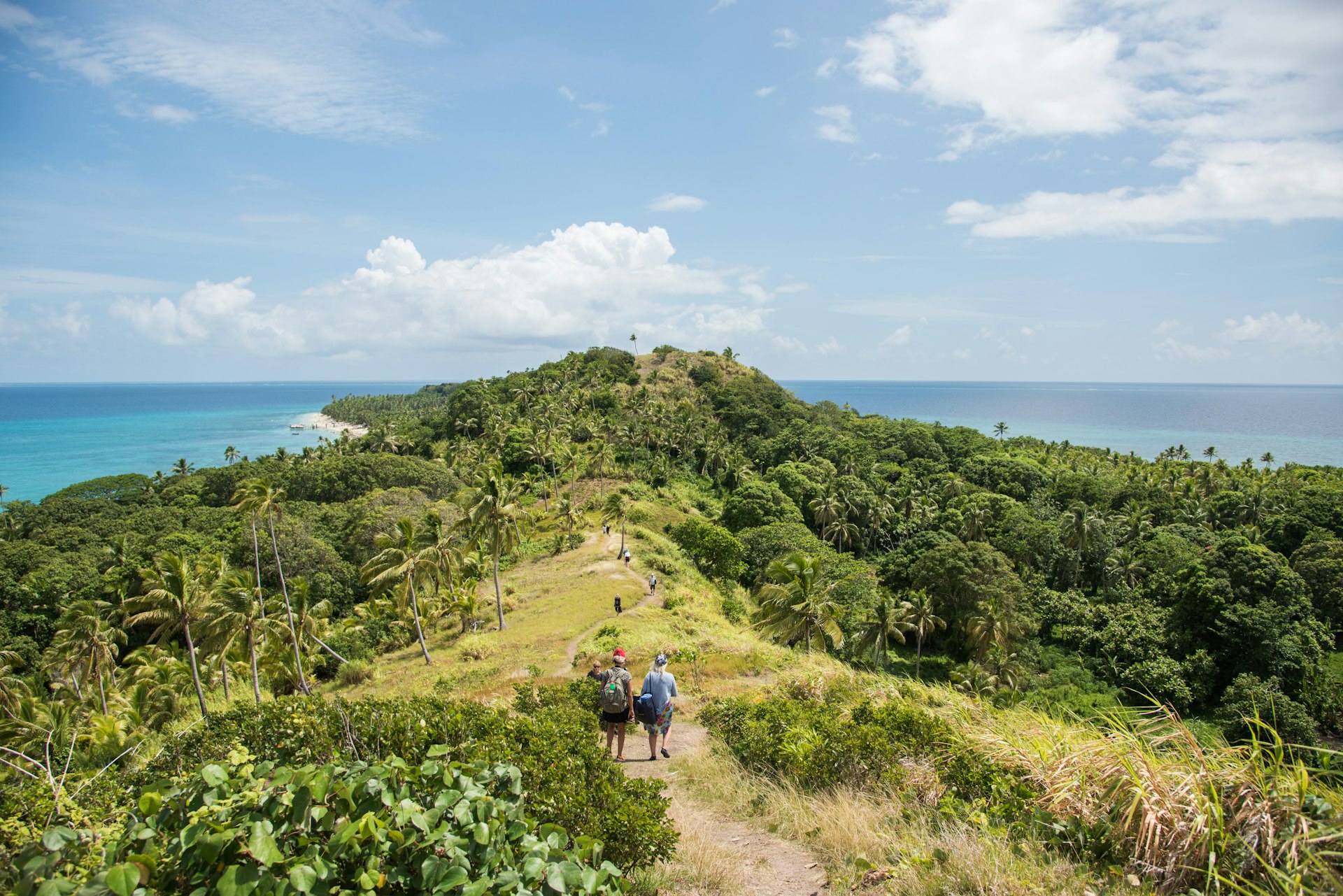 Tourists hiking along mountain ridge with lush greenery and Pacific Ocean seascape on Dravuni Island, Fiji