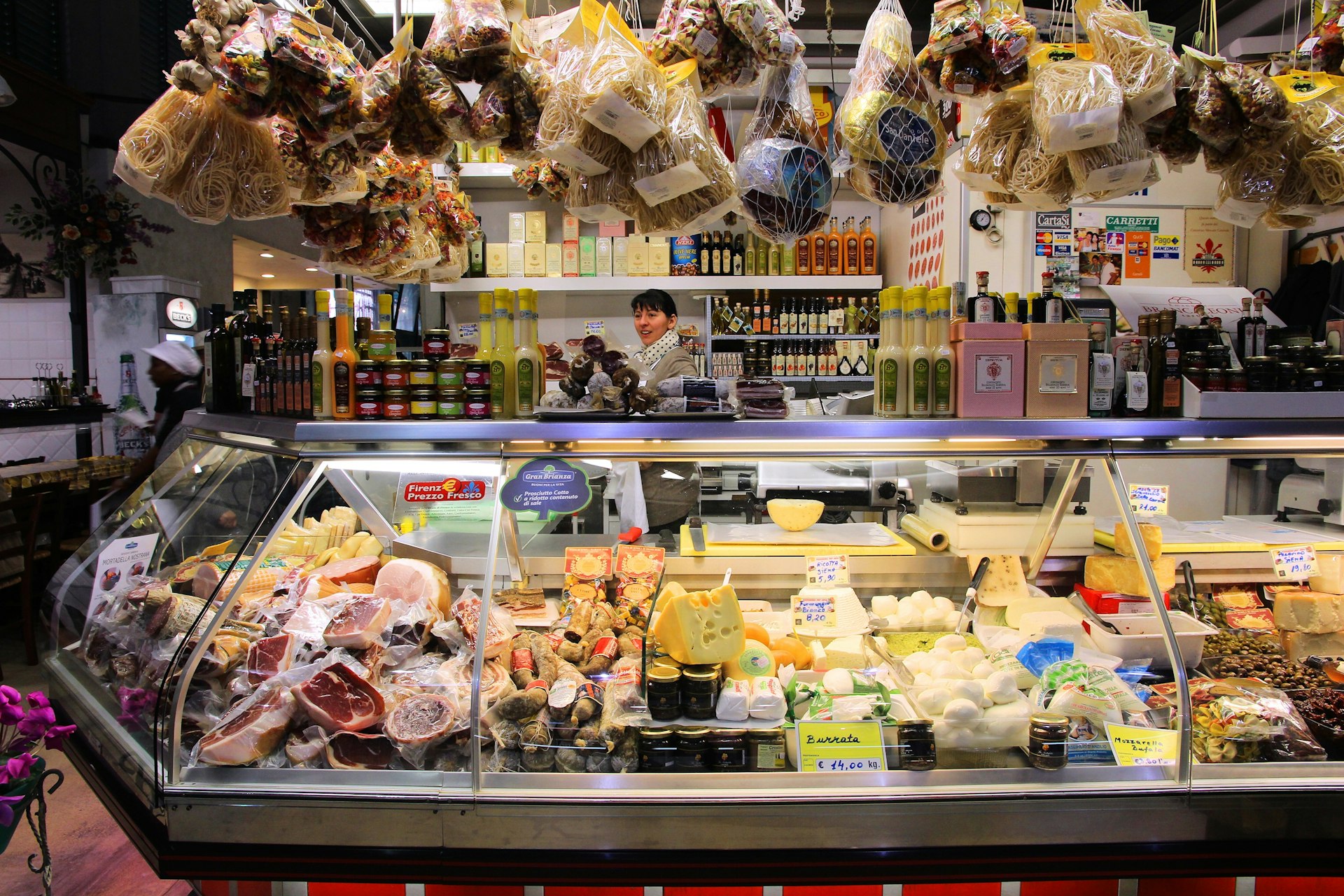 A vendor stands behind the refrigerated display counter of a stall selling cold meats, cheeses and dry goods in Florence's Mercato Centrale