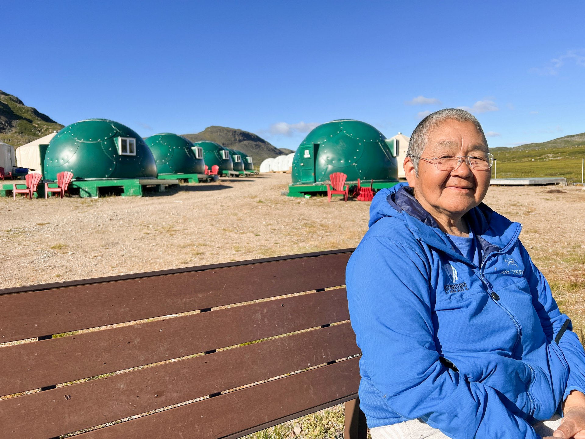A woman sits on a bench in front of round green structures that form part of Base Camp