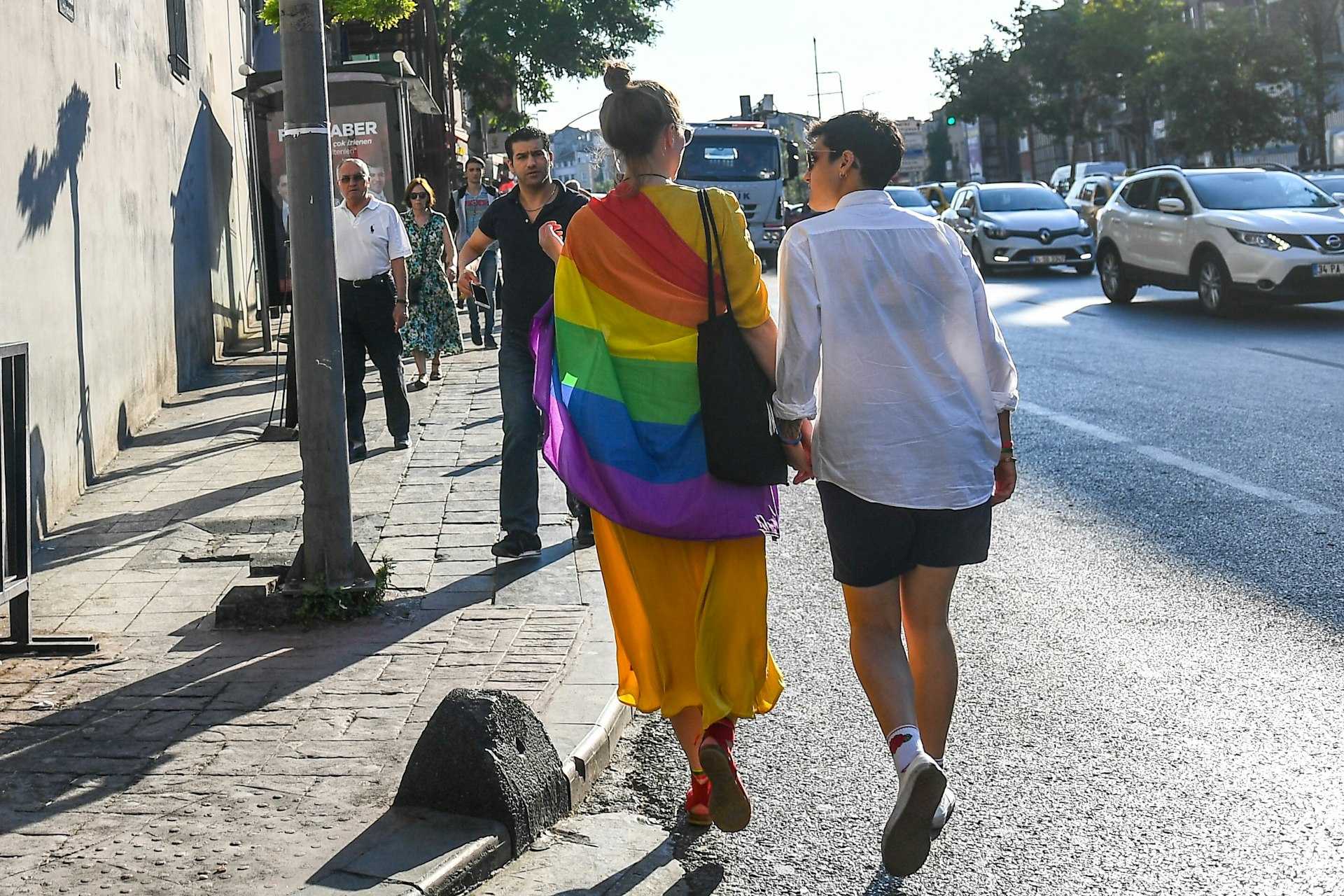 Two women holding hands and wrapped in LGBTQ Pride flag walk in Istanbul