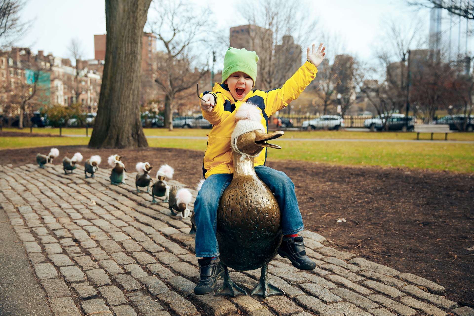 A small child sits on the back of a bronze duck sculpture and is clearly delighted with himself