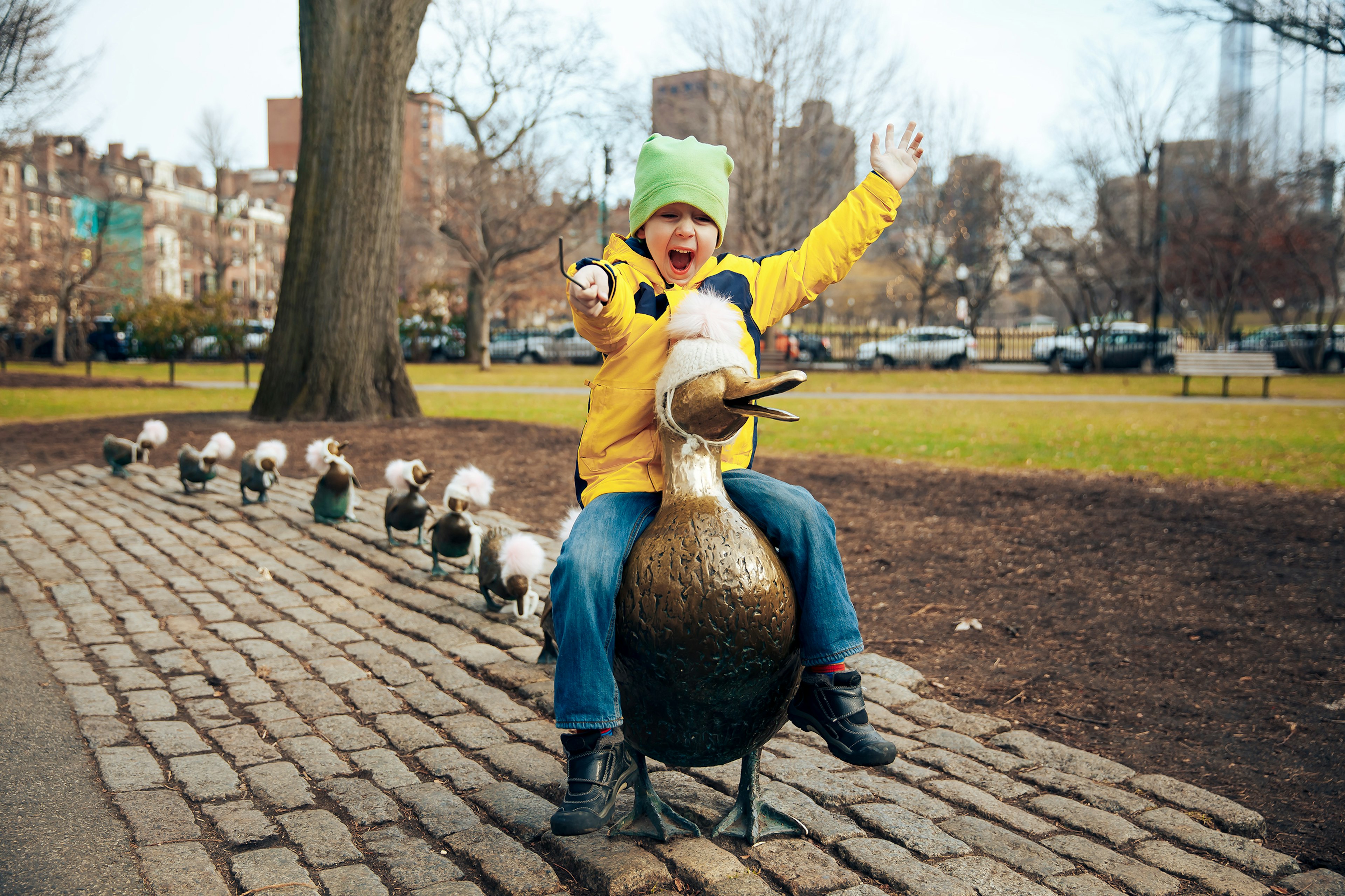 A small child sits on the back of a bronze duck sculpture and is clearly delighted with himself