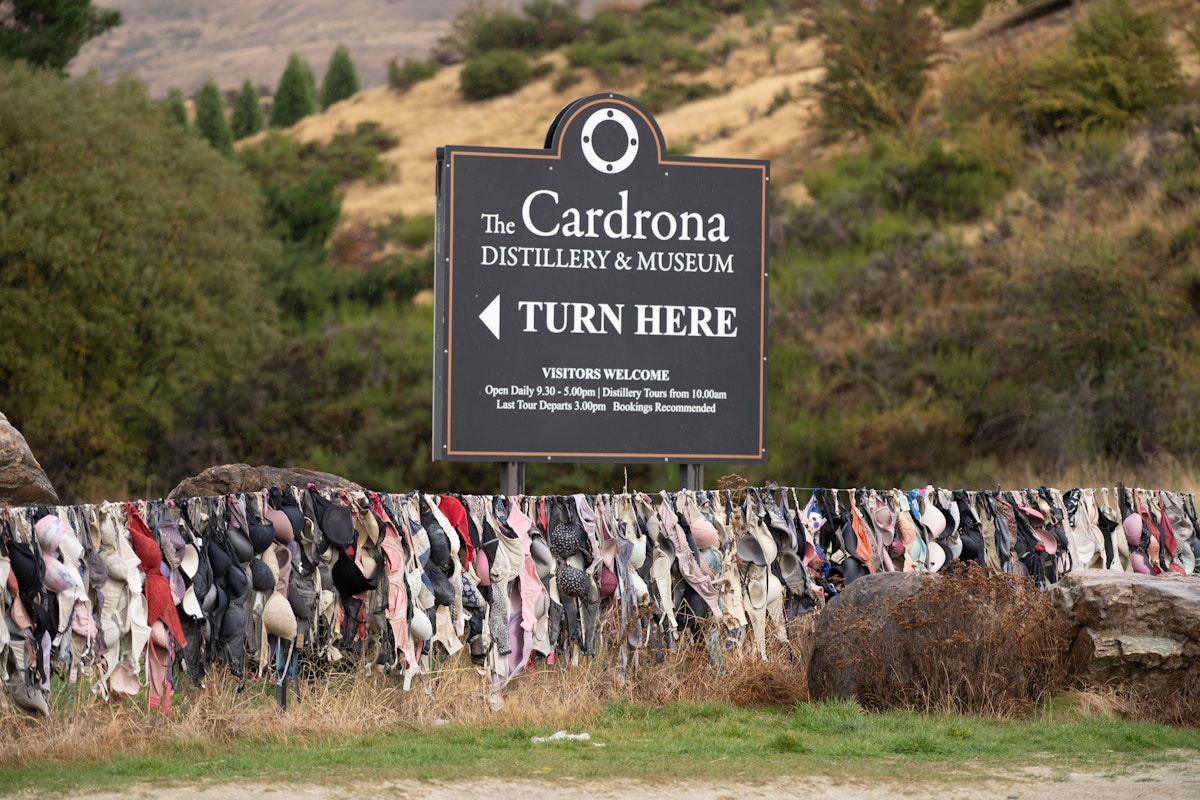 The Cardrona Distillery and Museum sign board with hundreds of bras hanging on the fence known as Bradrona.