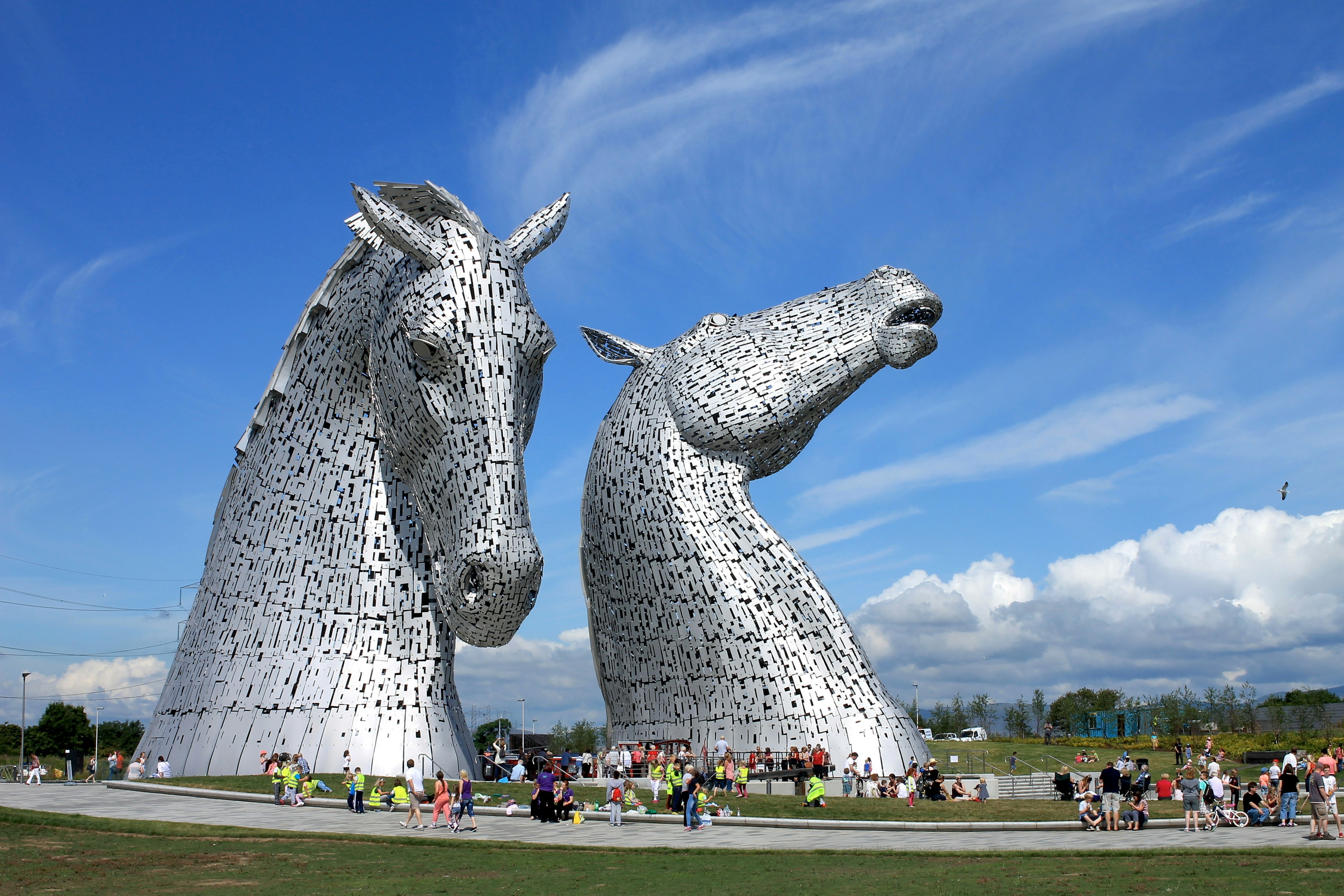 Two massive horse-head sculptures on the edge of a canal being visited by people