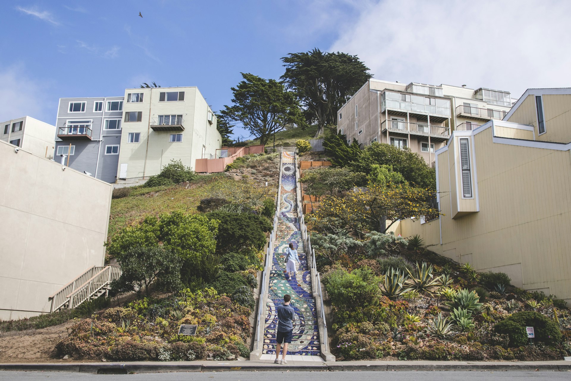 Two people being the long climb up a very high flight of stairs on a hillside in San Francisco, patterned with decorative tiles