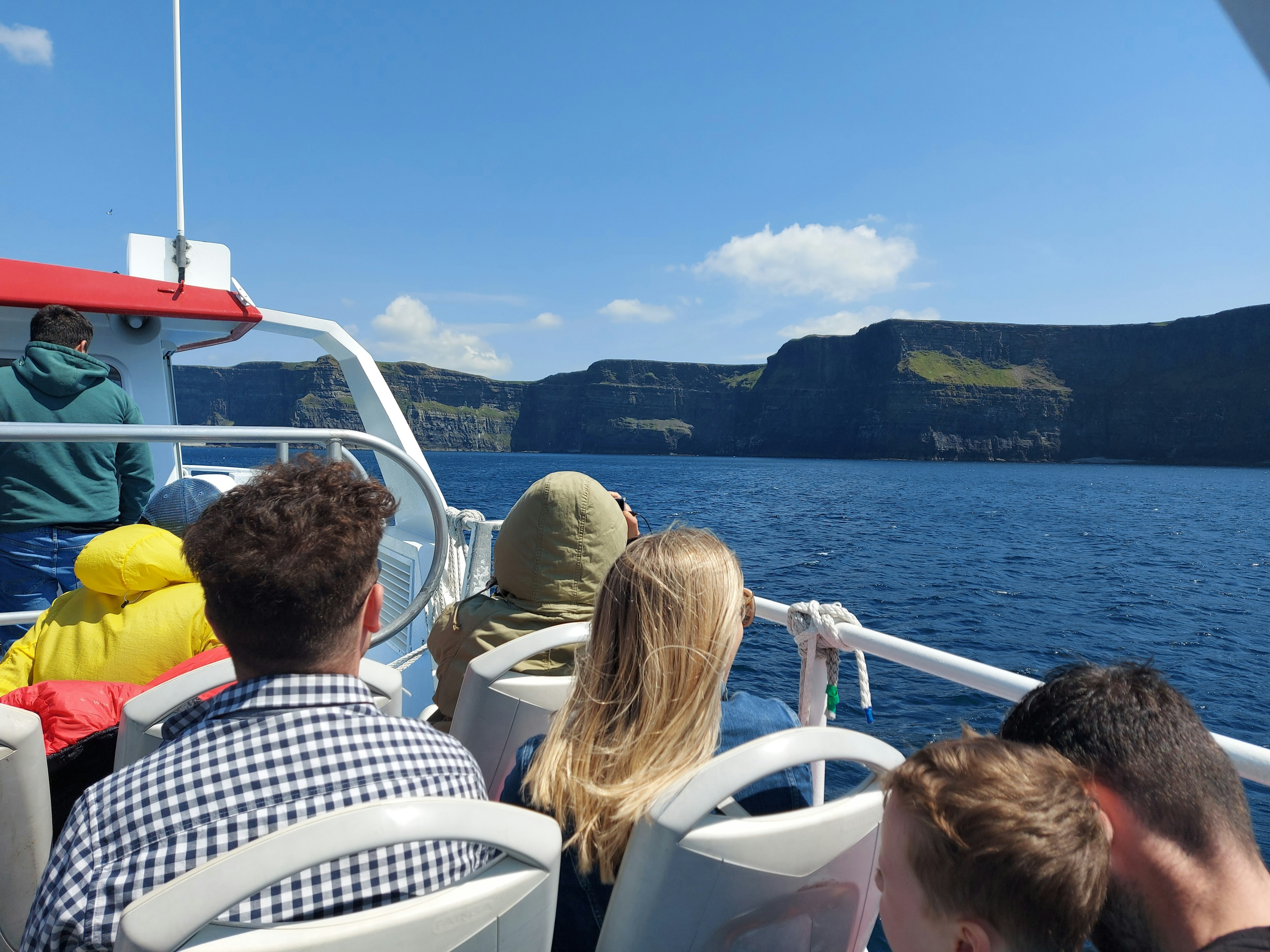 People on the top deck of a ferry admire the Cliffs of Moher, County Clare, Ireland