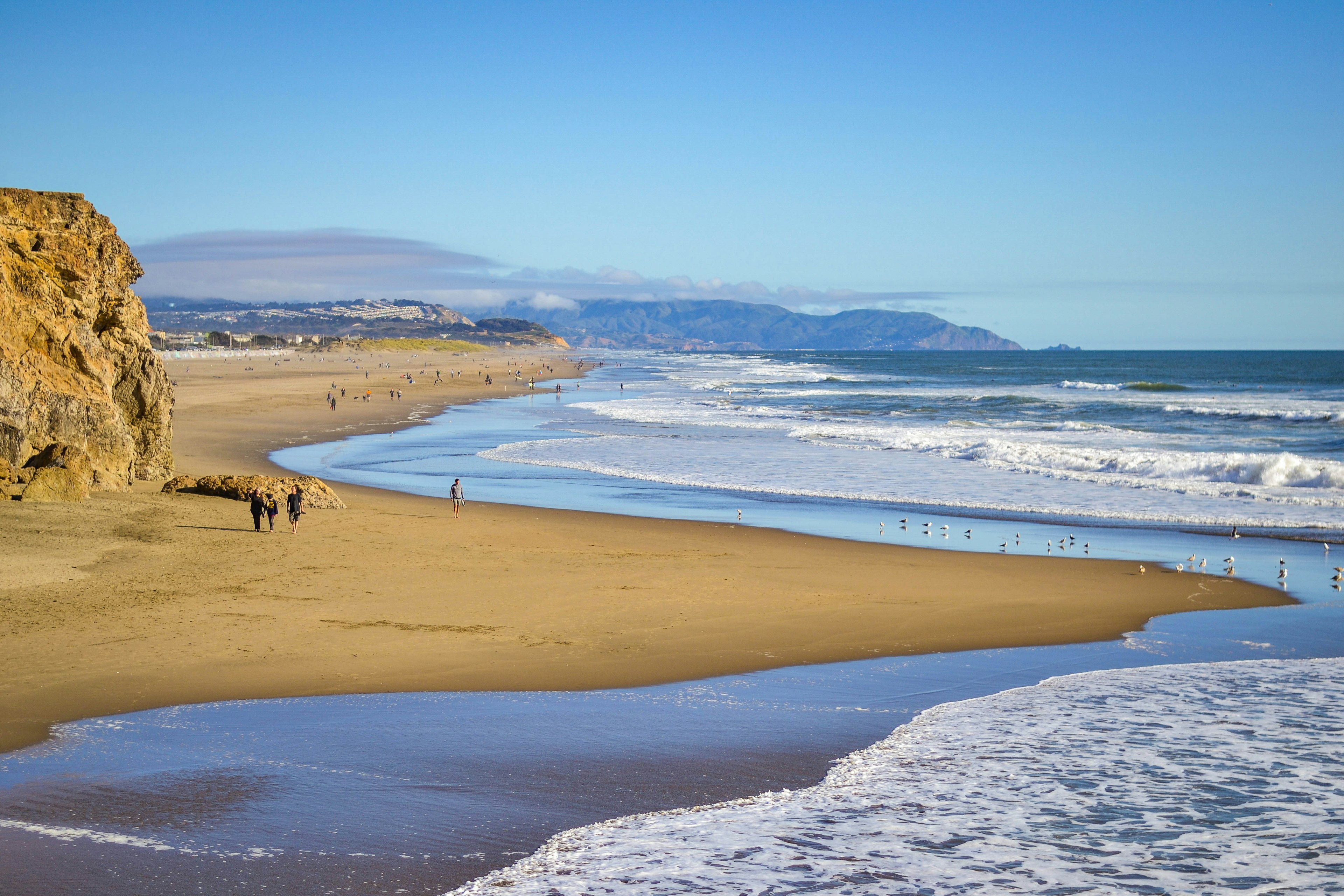 Shadowy figures wander a long a sandy beach on a windy day