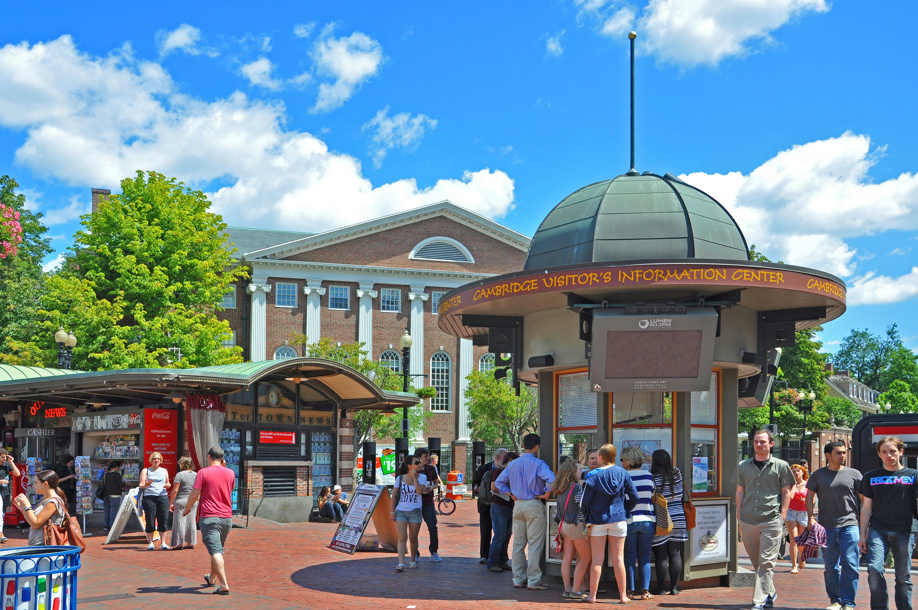 People mill around a square and information center outside a grand building