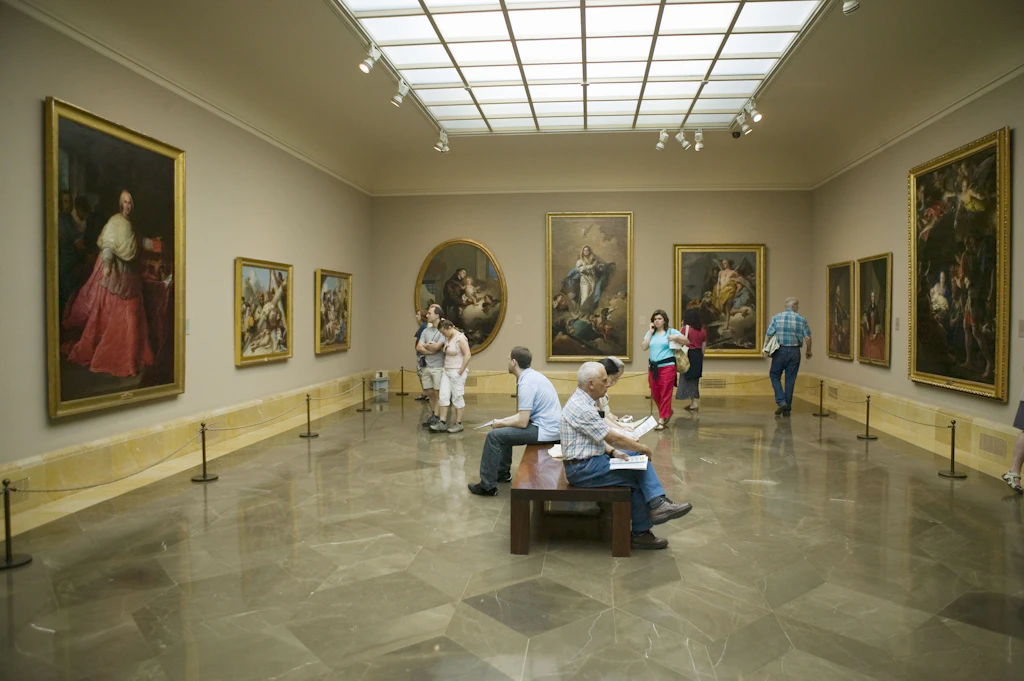 Museo del Prado, Madrid People sit on a central bench while others walk around a gallery lined with large paintings