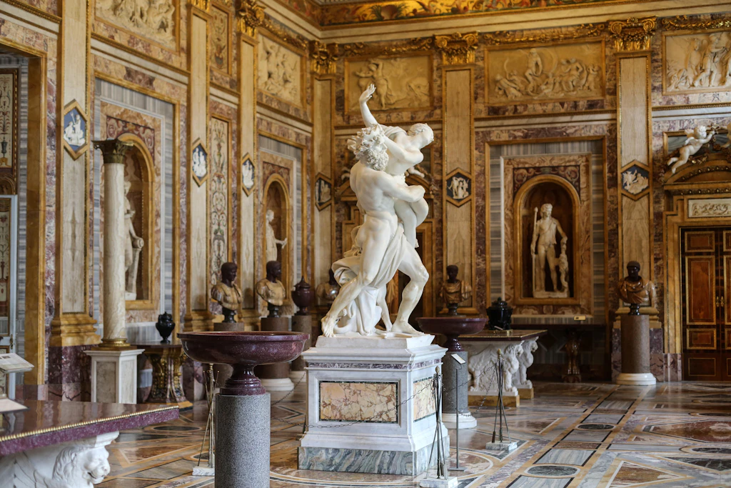 Rape of Proserpine in Galleria Borghese, Rome A large marble statue of a male figure grabbing a female stands in the center of a gallery