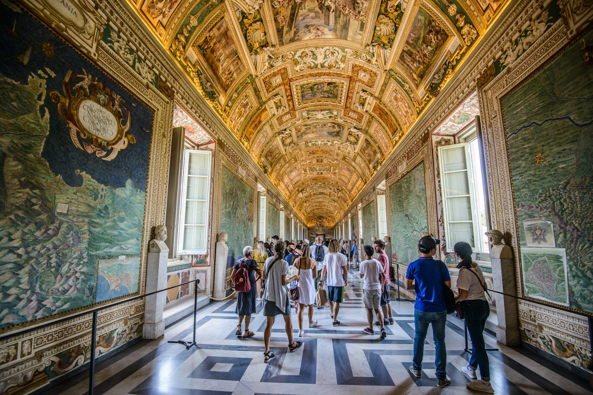 Visitors walk under frescoes in a hallway at the Vatican Museum, Rome, Italy
