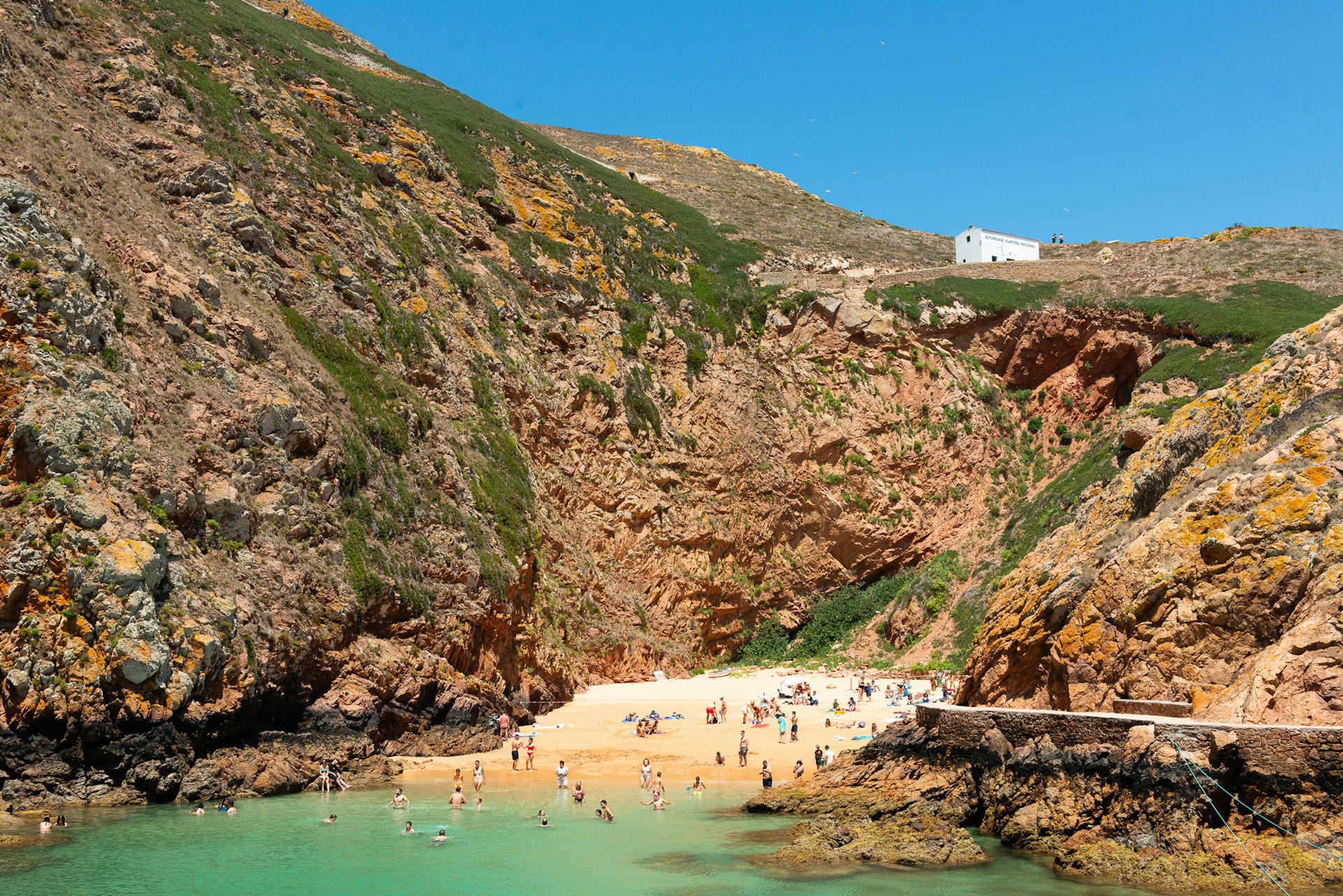 People play on the beach and swim in the turquoise waters of a secluded cove backed by large rocks