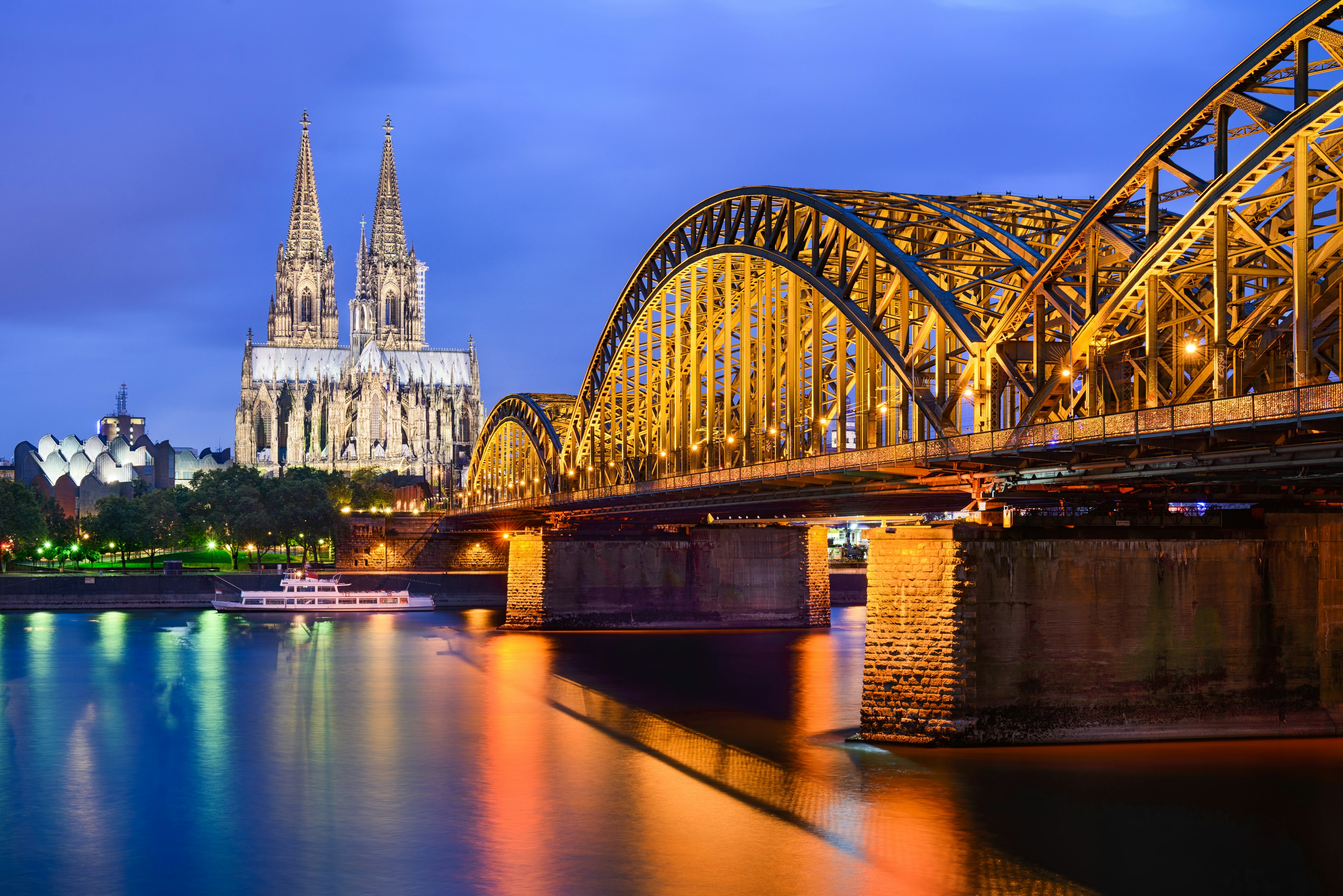 Illuminated view of a large cathedral next to a river with a bridge crossing