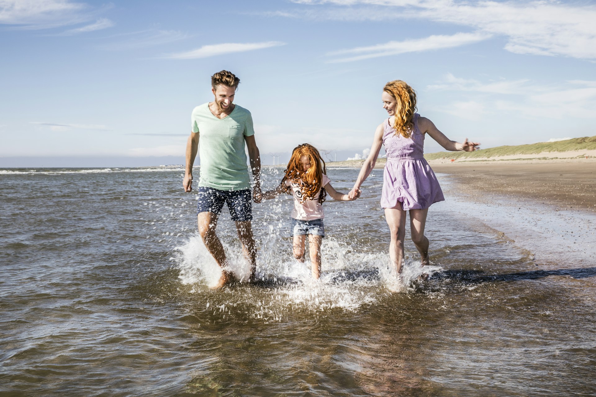 A family of three splash through the shallows of the sea on a day at the beach
