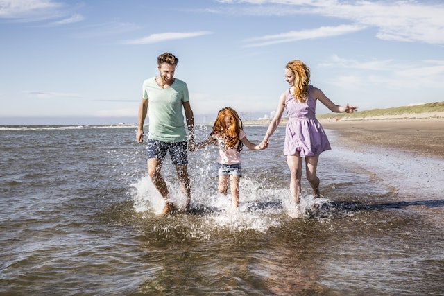 A family of three splash through the shallows of the sea on a day at the beach