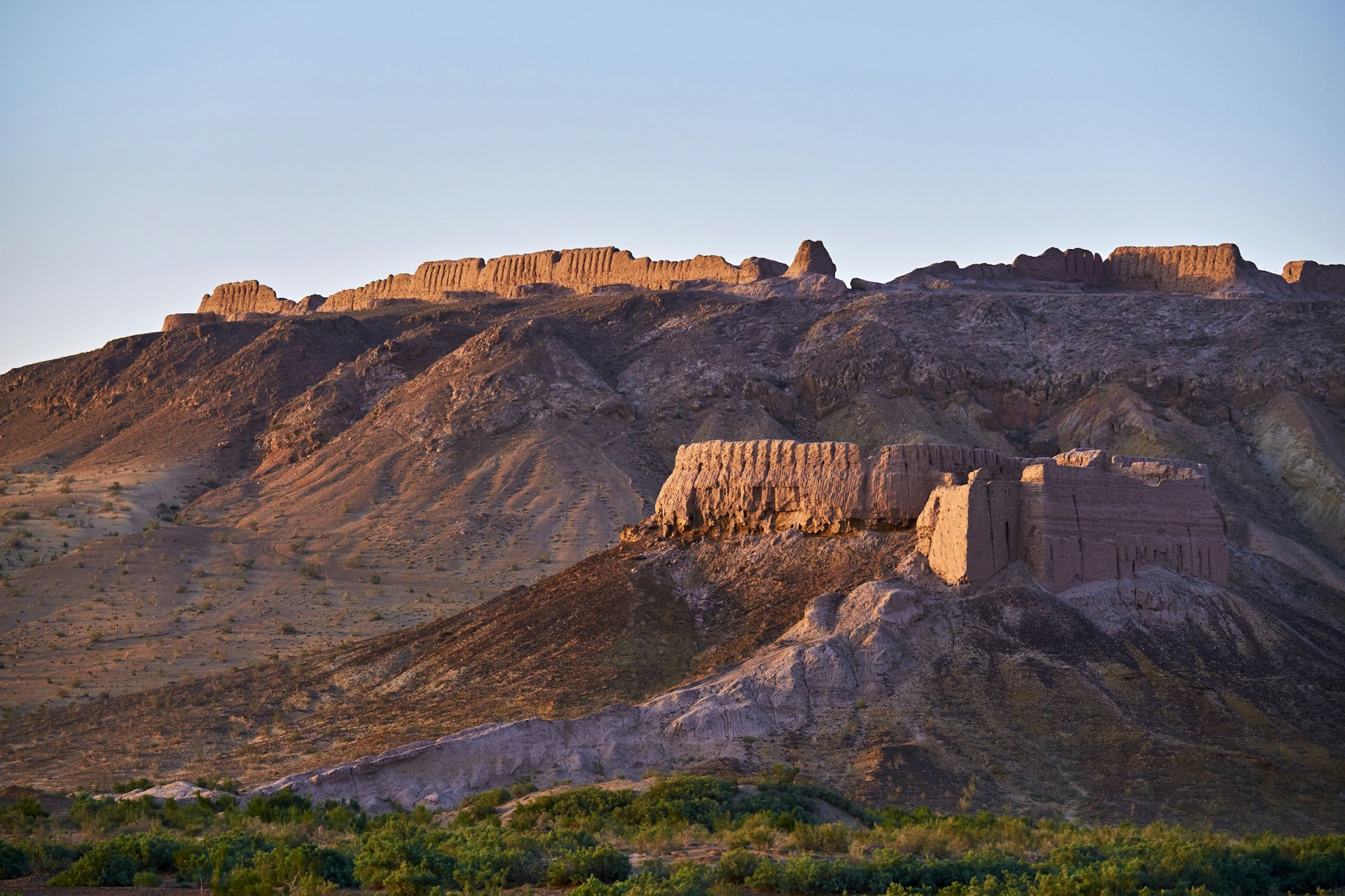 A red-stone ruined medieval fortress stands on the top of a cliff in a desert area