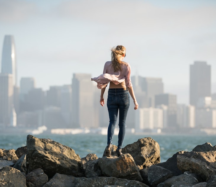 Young woman standing on rocks with the San Francisco skyline in the background.
1164629701