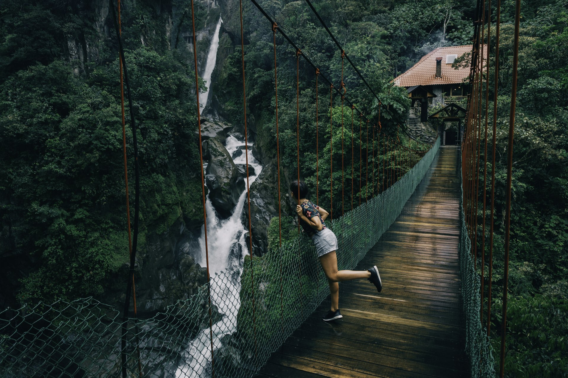 Woman wearing shorts on a suspension bridge looking to a waterfall in Ecuador
