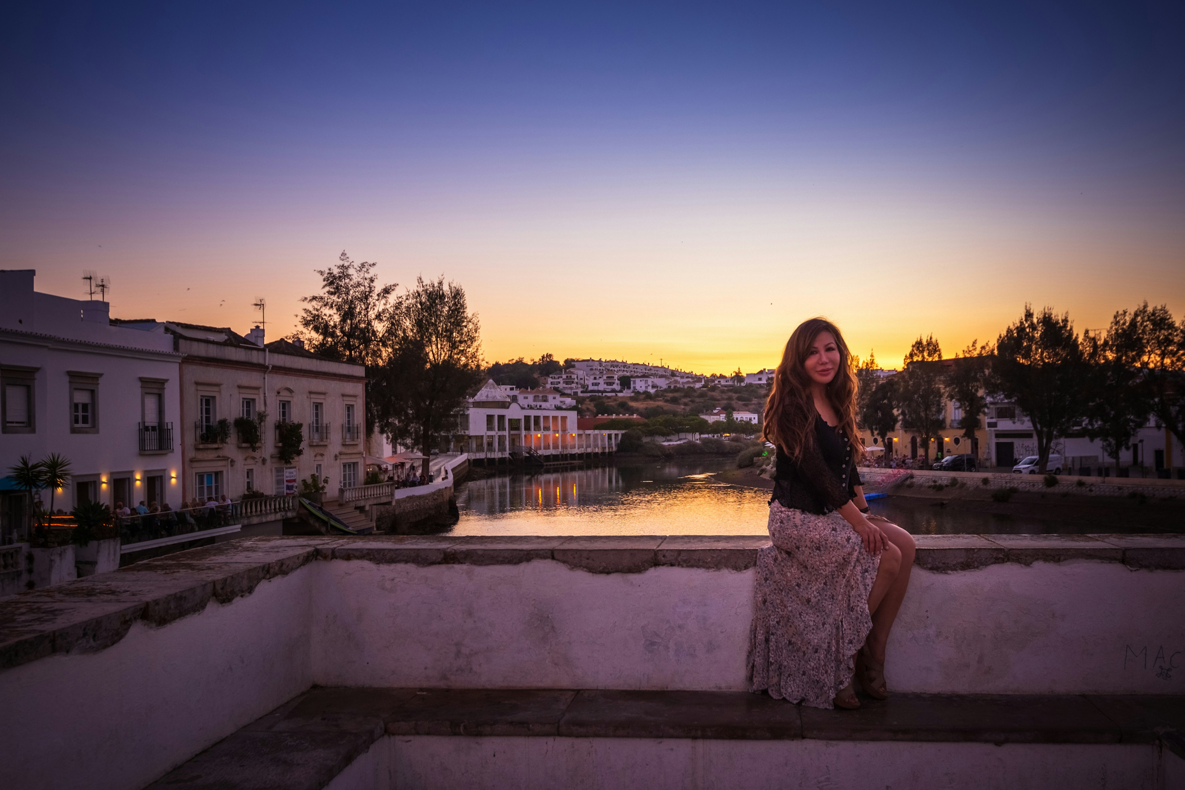 A woman sits on a riverside at sunset