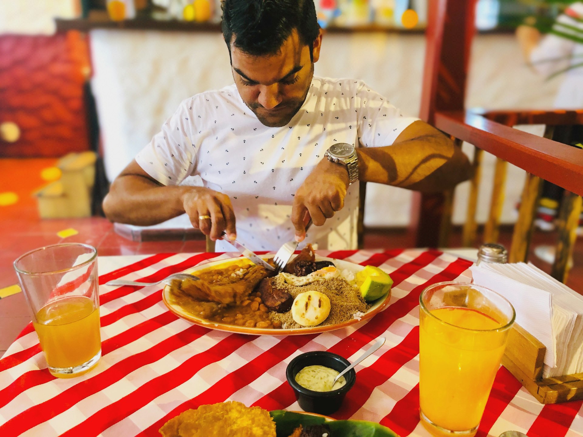 A man tucks into a large plate of food including rice, beans, pork rinds, ground beef, sausage, egg, black pudding, avocado, grilled plantain and arepa
