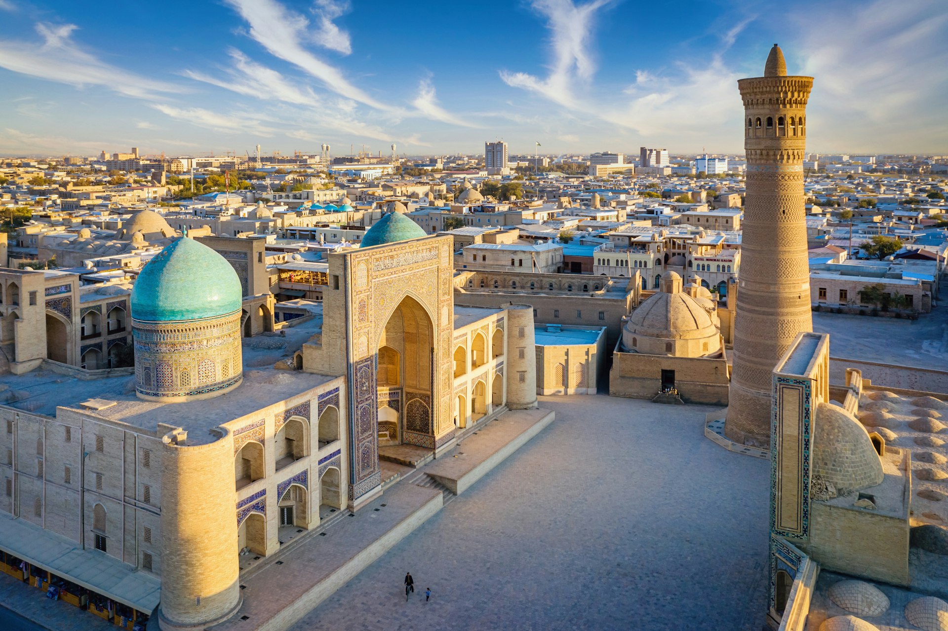 A complex of mosque buildings with two blue tiled domes and a tall minaret