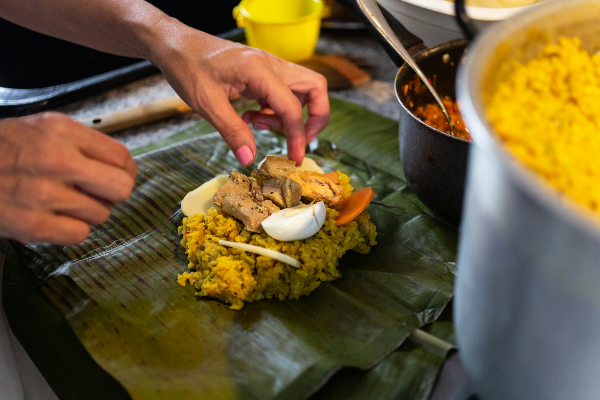 Woman cooking traditional Colombian food, tamales, laying out the ingredients on a green banana leaf