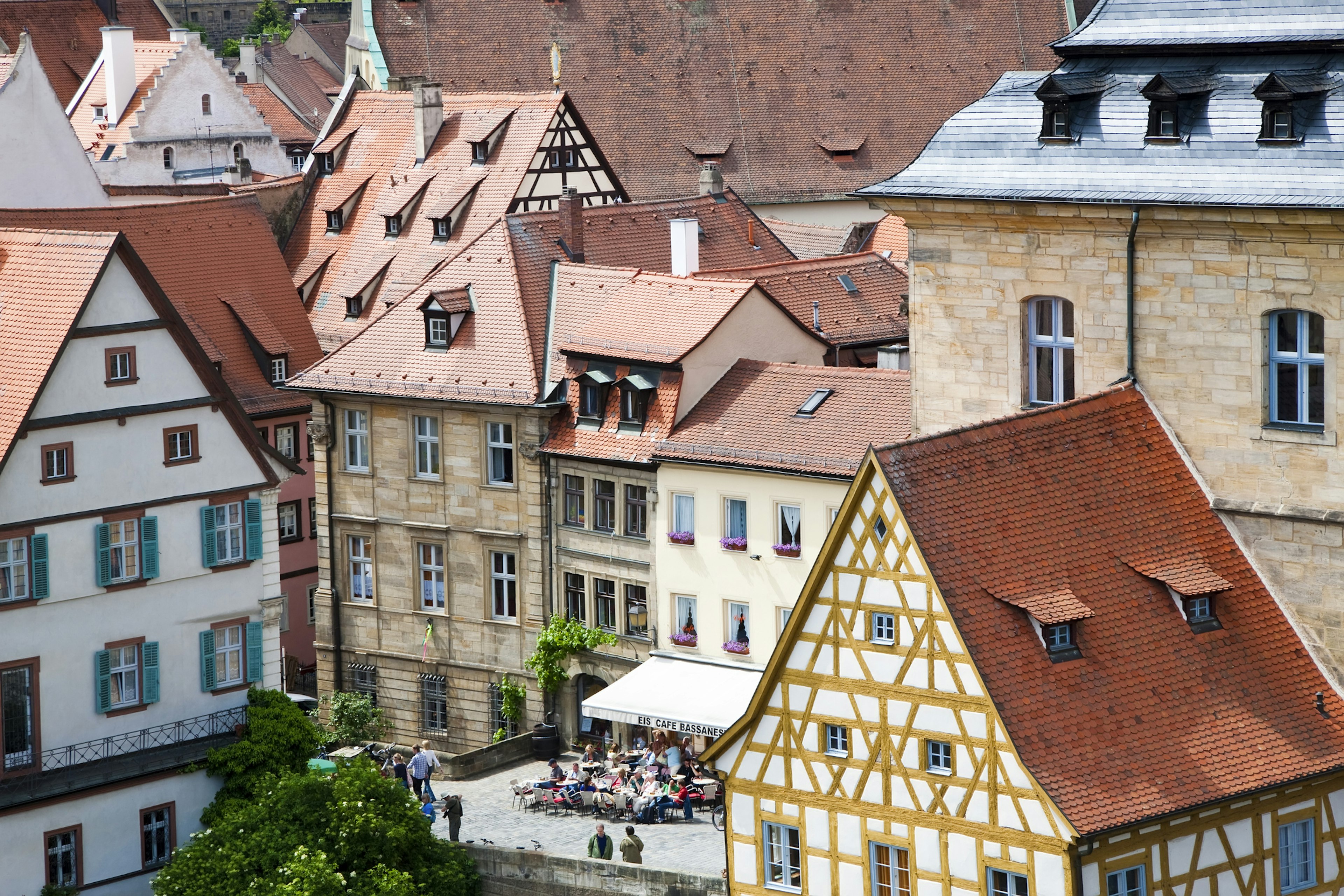 Red-tiled rooftops lead down to a city square where people are having a drink outside a cafe