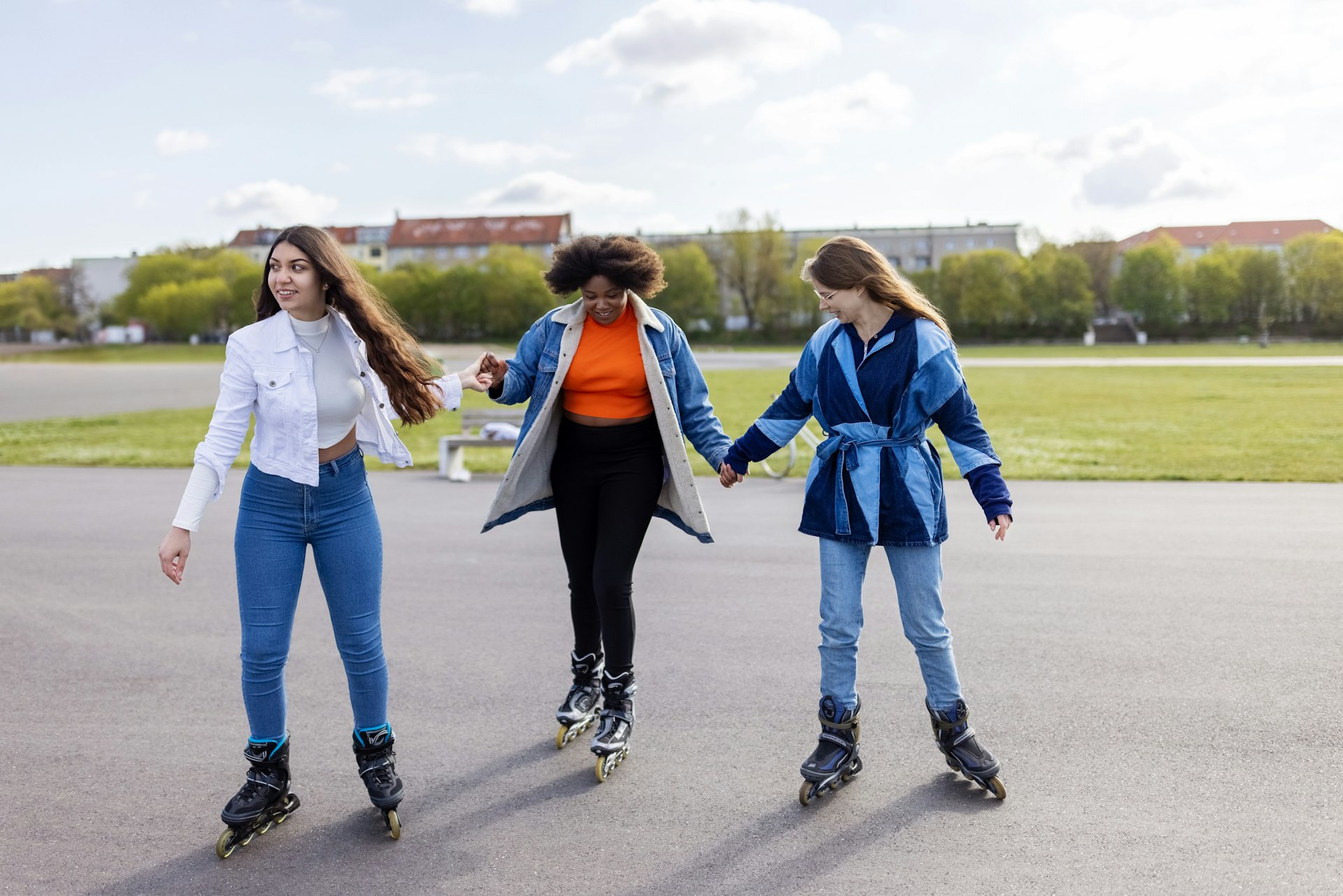 Three teenage girls roller-skate on the runway of a former airport, now a vast park in Berlin