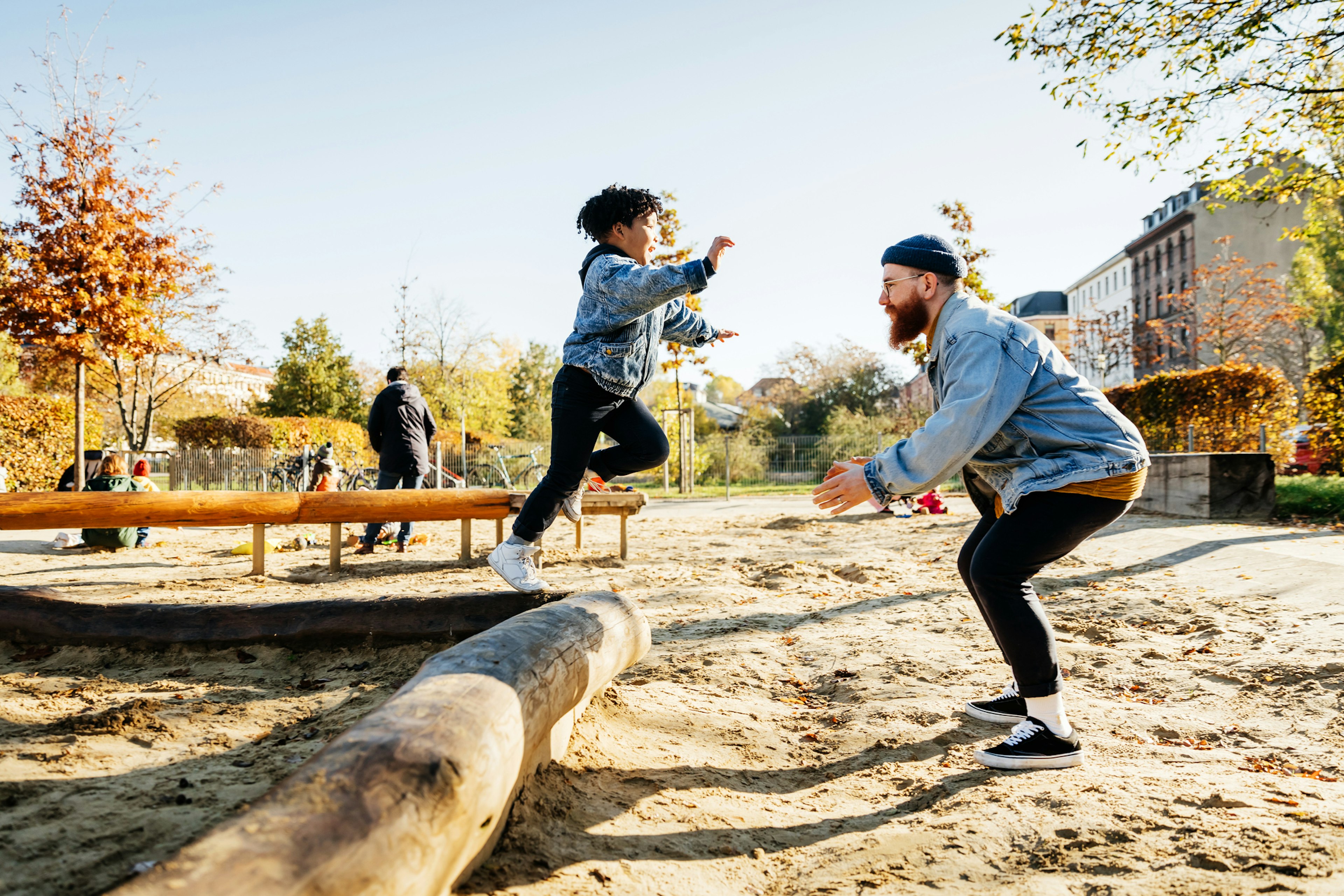 A young boy leaps into his father's arms from a log while messing around in a playground at the park together