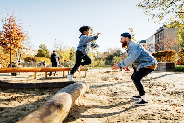 A young boy leaps into his father's arms from a log while messing around in a playground at the park together