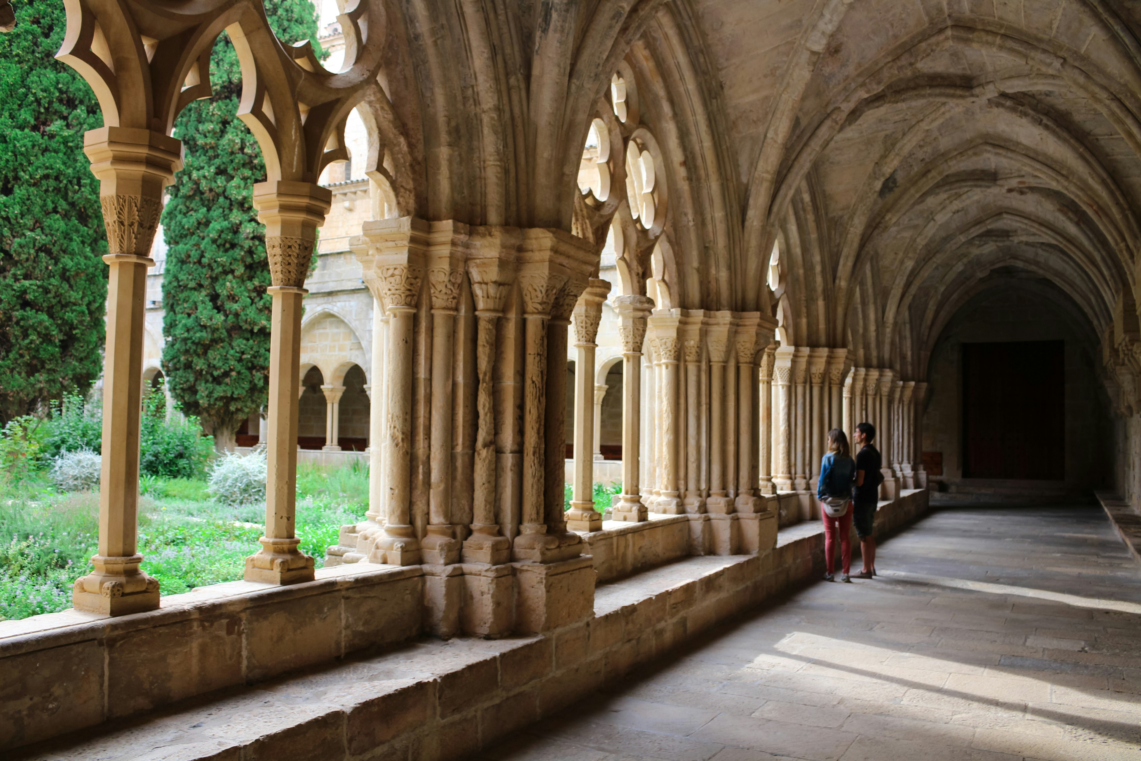 Two people standing in an arcade, looking out through arched stone columns at the landscape behind