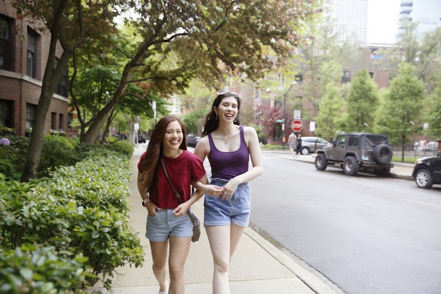 Two young women walking arm-in-arm and laughing on a street in Chicago