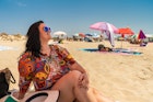 A woman smiling while sitting on the beach at  Praia do Barril in Tavira, Portugal