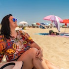 A woman smiling while sitting on the beach at  Praia do Barril in Tavira, Portugal