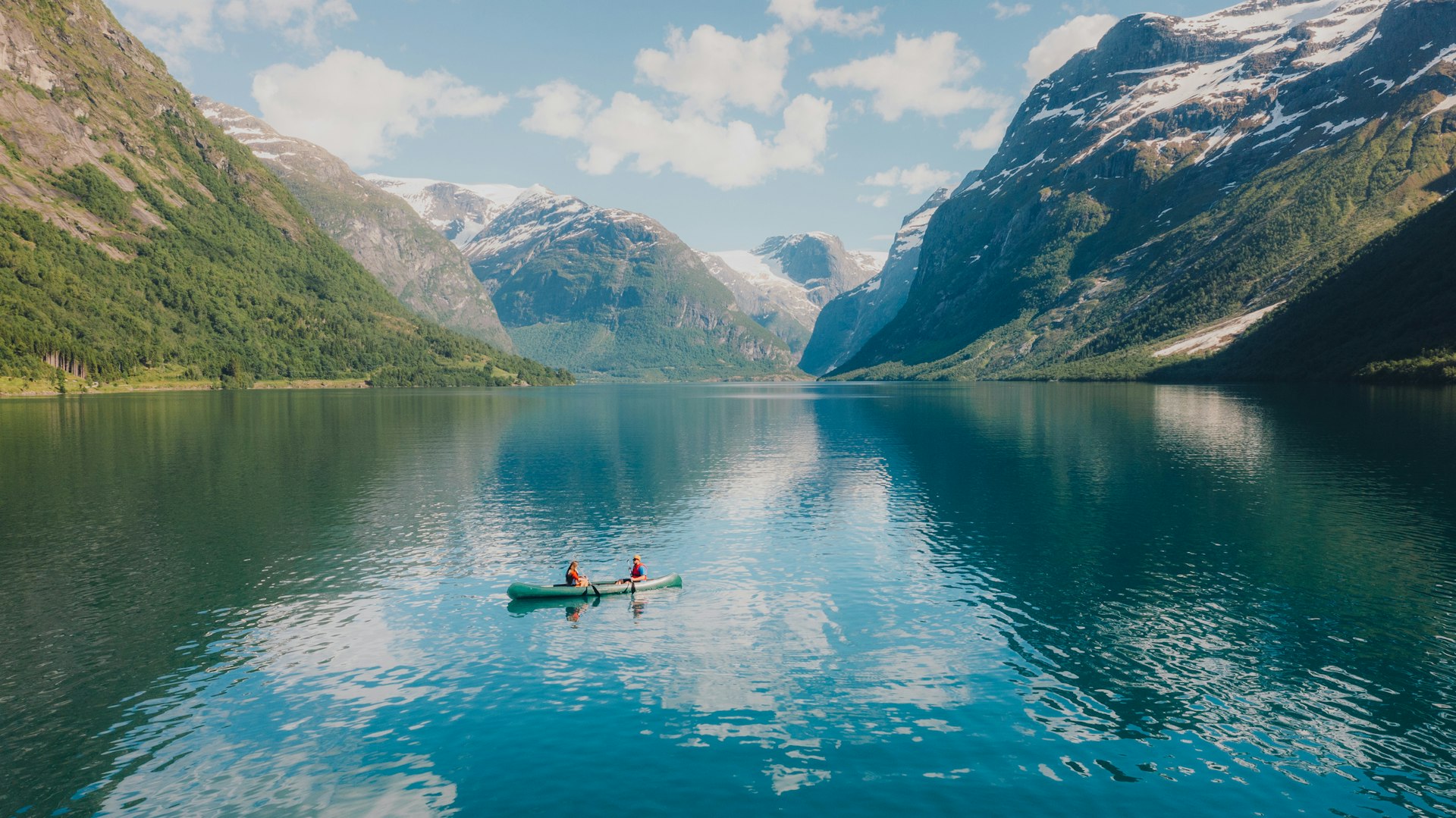 Couple sailing in a canoe in a crystal blue glacier lake surrounded by snowcapped mountains