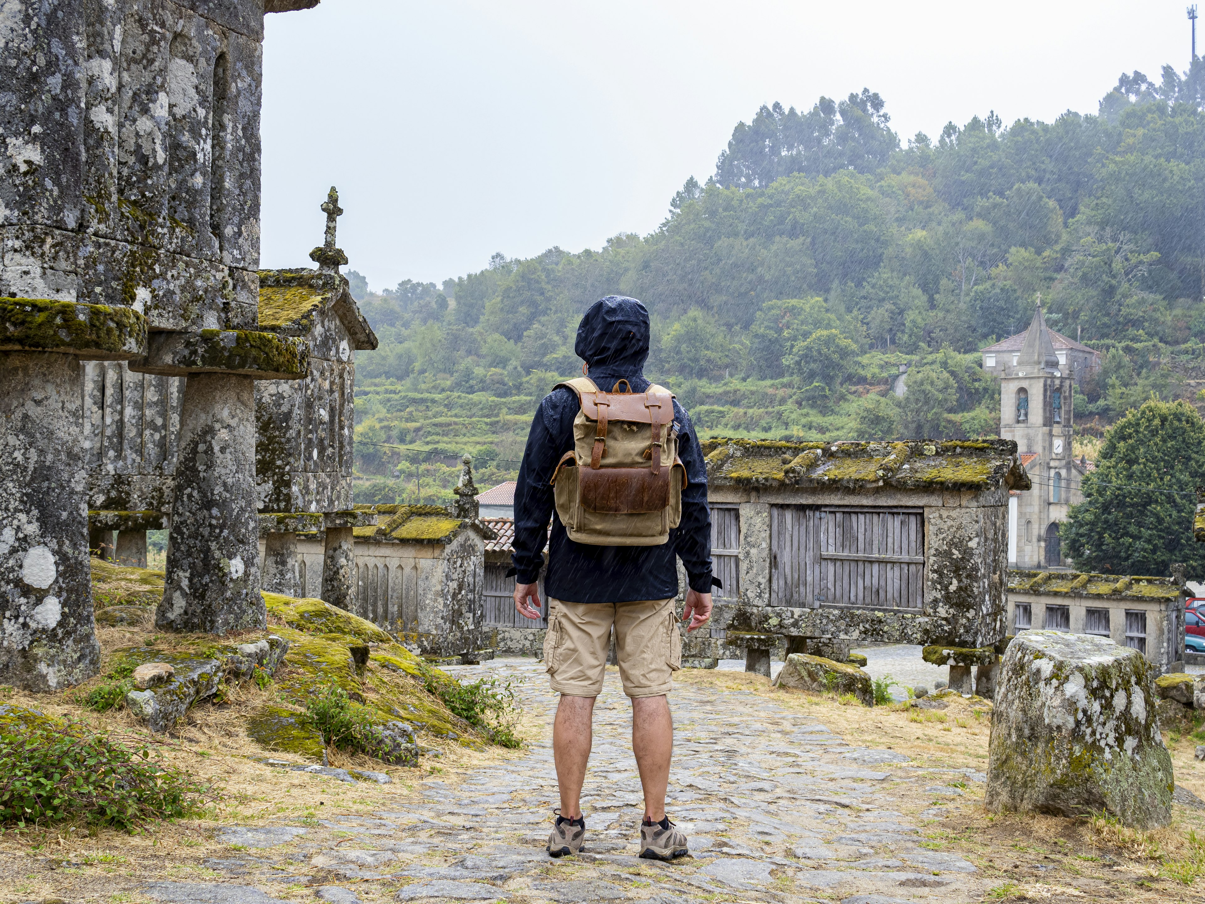 Man on his back looking at the historic stone barns in the town of Lindoso in Portugal as it rains.