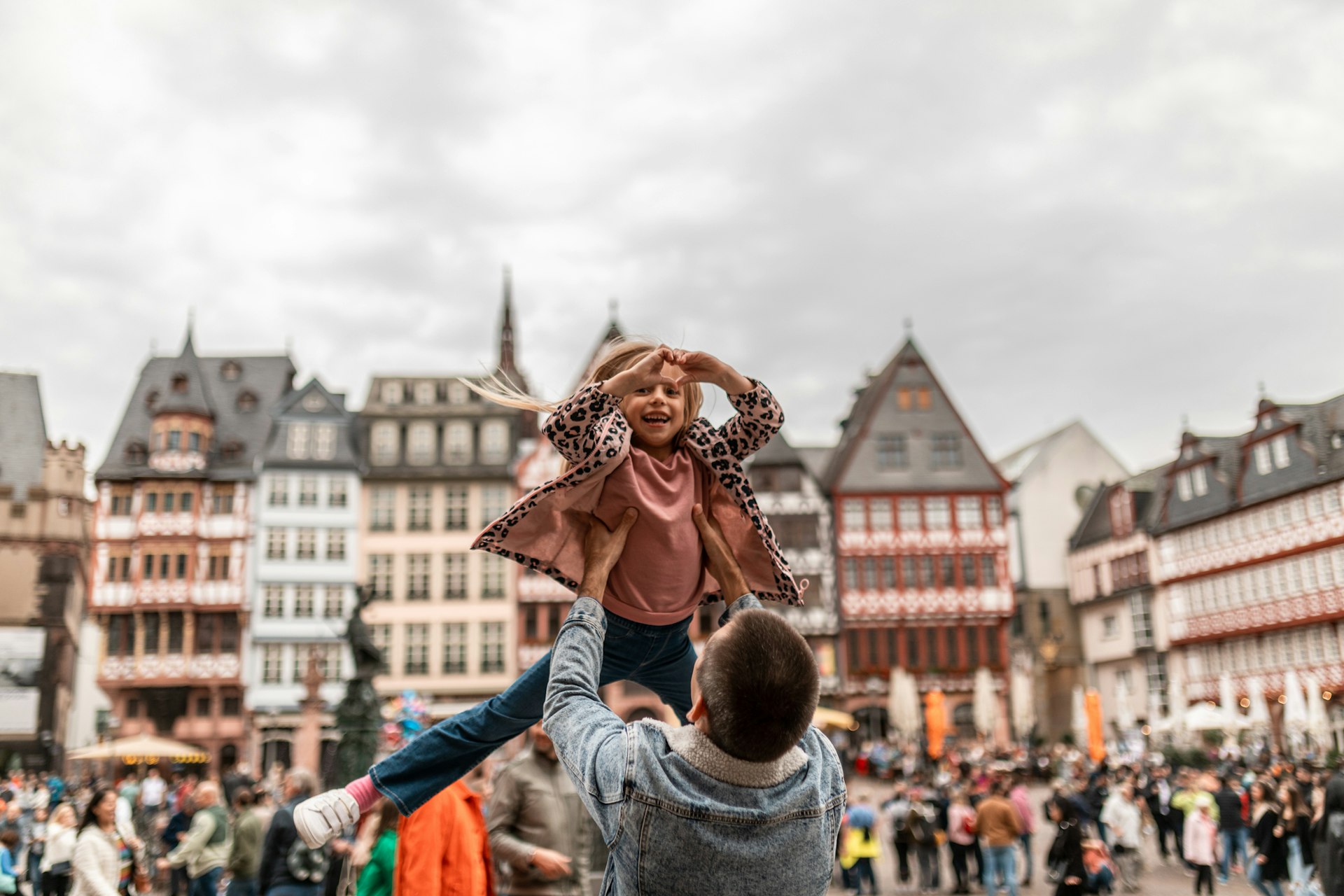 A father throws his daughter in the air in a town lined with half-timbered houses