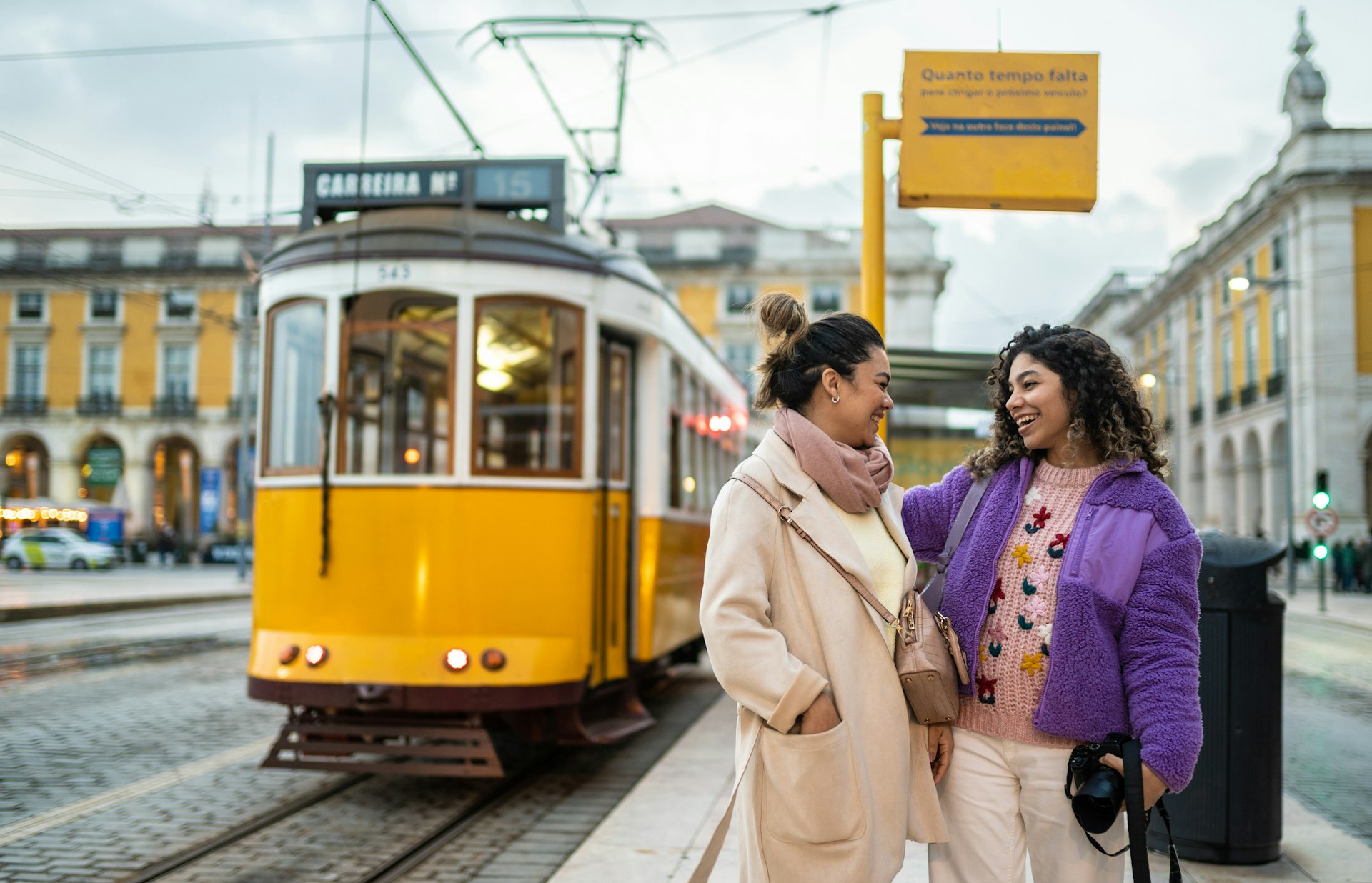 Two women laughing together next to a tram stop in Lisbon